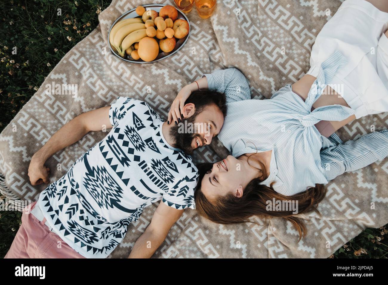 Top-Down-Bild von einem fröhlichen Mann und einer kaukasischen Frau, die auf einer Decke liegen und gemeinsam ein Picknick am Wochenende genießen, und einem glücklichen Paar mittleren Alters, das ein Picknick macht Stockfoto