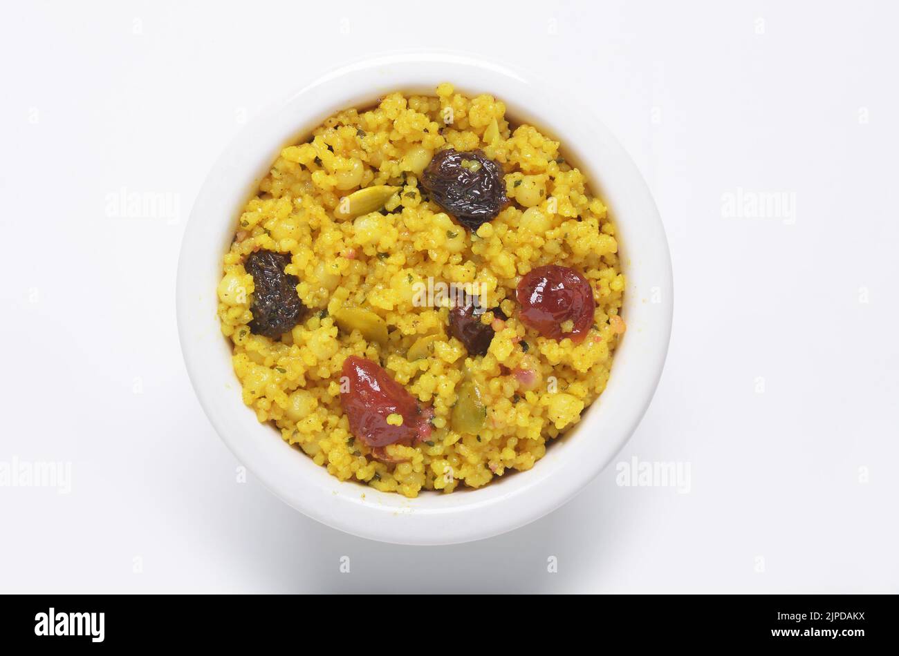 Marokkanischer Couscous mit Rosinen, Preiselbeeren und Kürbiskernen in einer weißen Keramikschale, die von direkt oben auf weißem Hintergrund aufgeschnitten wurde Stockfoto