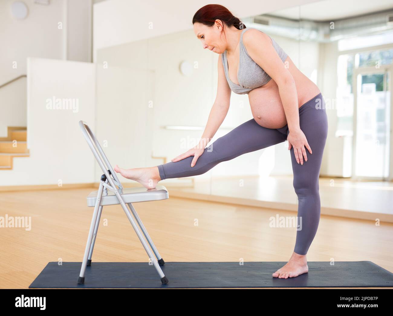 Eine Schwangerin ist im Yoga engagiert. Stuhlübungen Stockfoto