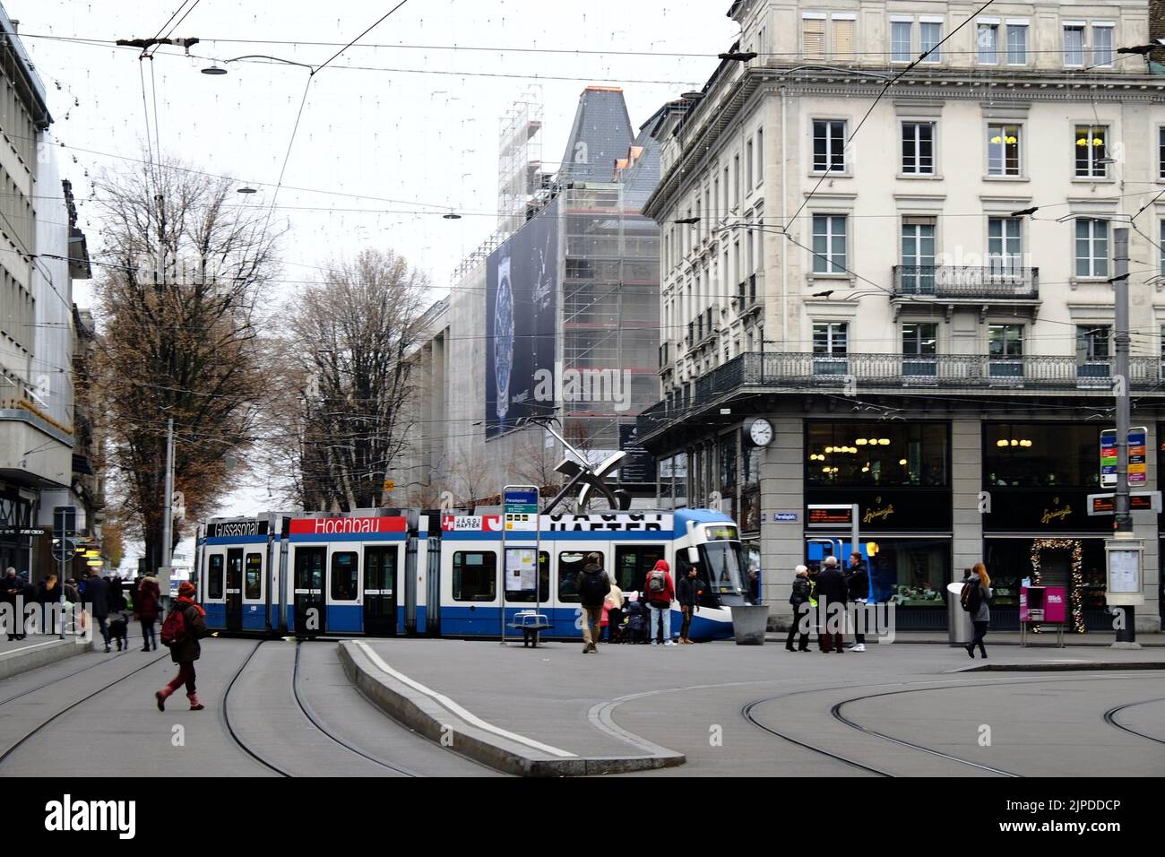 Eine blaue Straßenbahn gegen das Stadtbild in der Schweiz mit Menschen, die herumlaufen Stockfoto