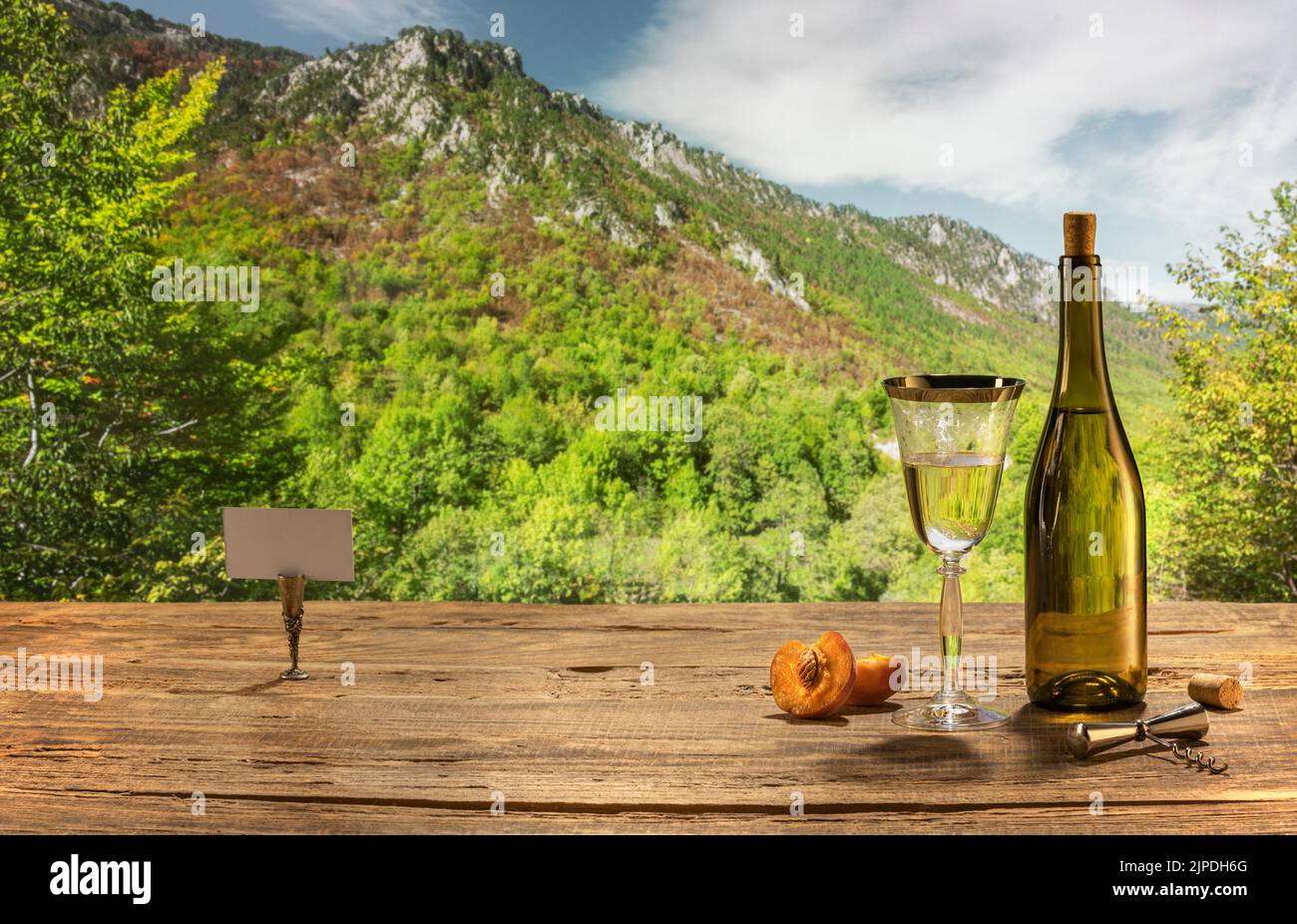 Sommerurlaub. Dunkle Flasche weißen trockenen Wein in Glas gegossen, auf Holztisch isoliert über Berglandschaft. Stockfoto