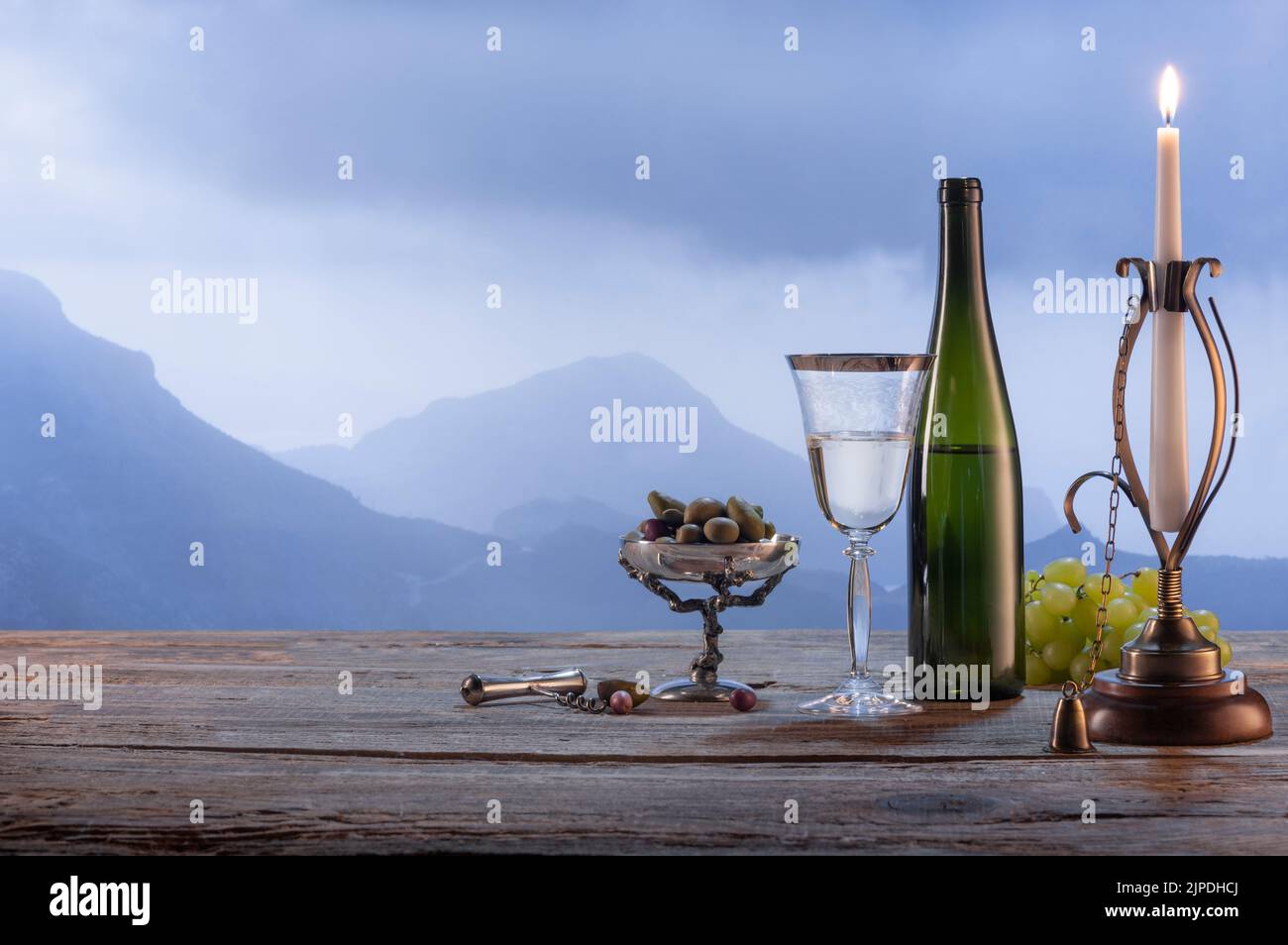 Natürlicher Blick. Eine Flasche Weißwein mit Oliven-Vorspeisen, die auf einem Holztisch stehen, isoliert über einem nebligen Berghintergrund Stockfoto