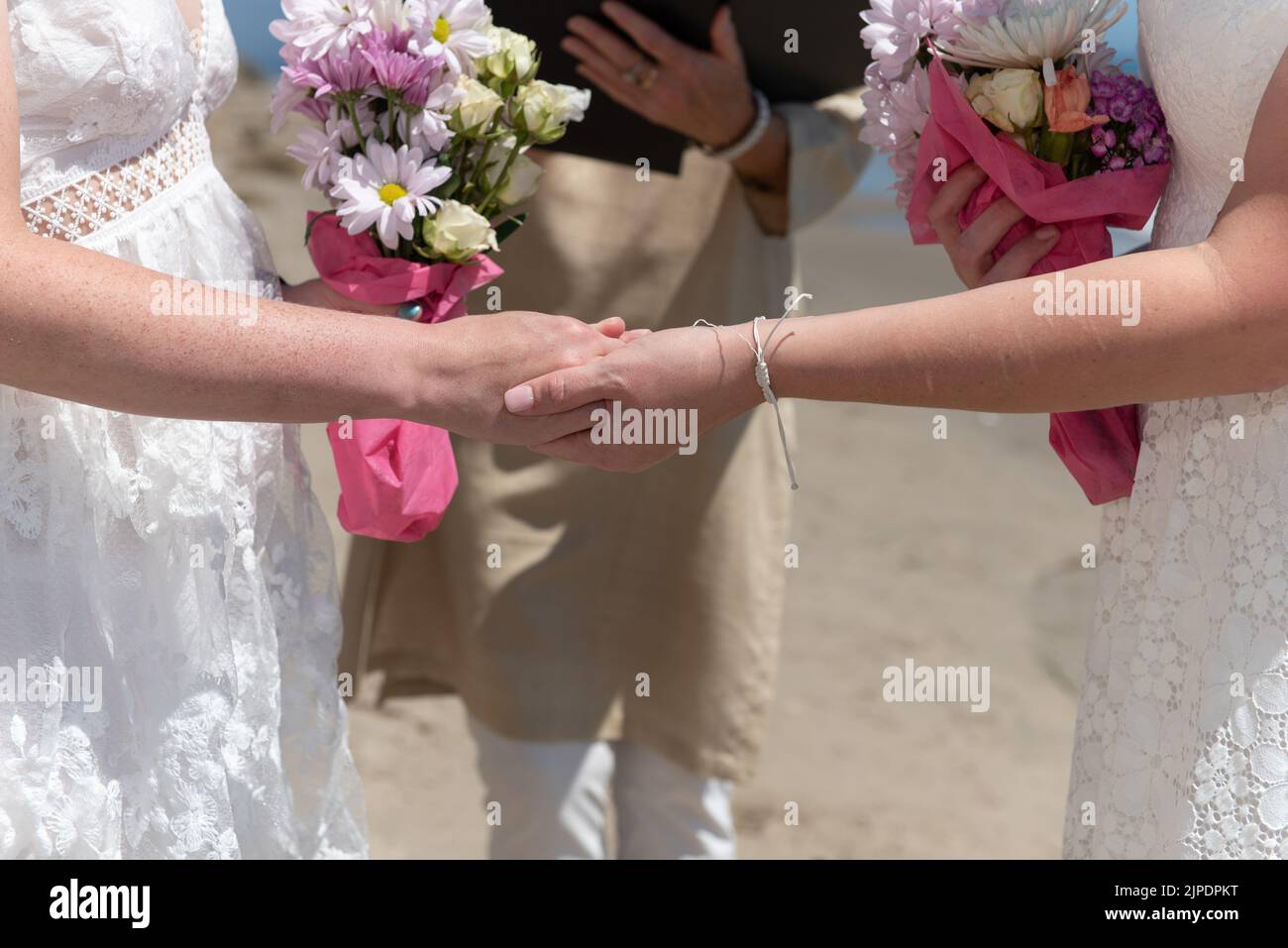 Bräute halten sich die Hände, während sie während der Hochzeitszeremonie ihre Liebe zueinander mit dem Amtsträger zum Ausdruck bringen. Stockfoto