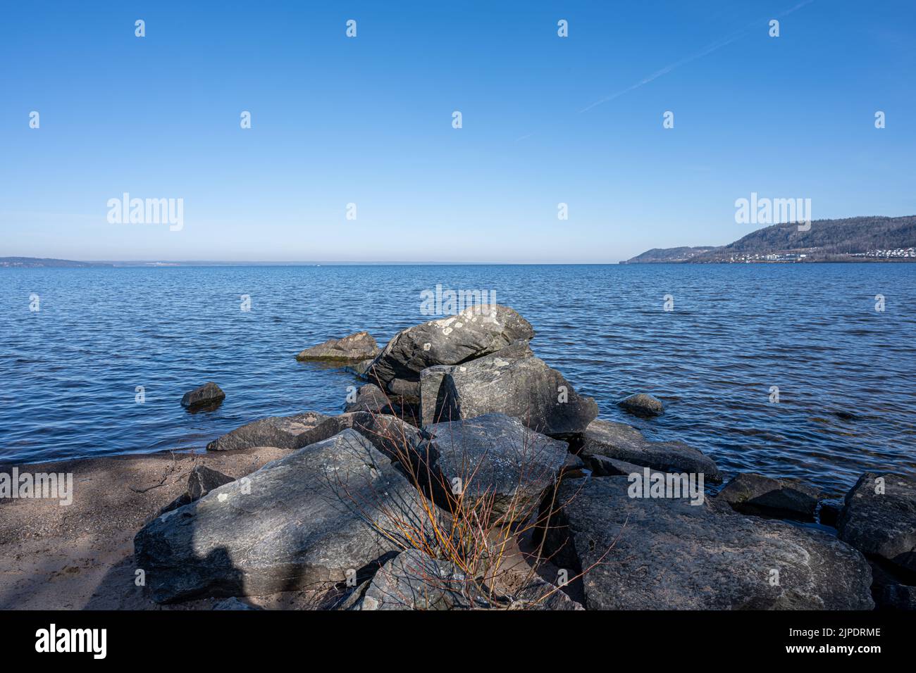 Felsbrocken als Teil eines Wellenbrechers in einem See. Bild vom See Vattern, Schweden. Blaues Wasser und Himmel im Hintergrund Stockfoto