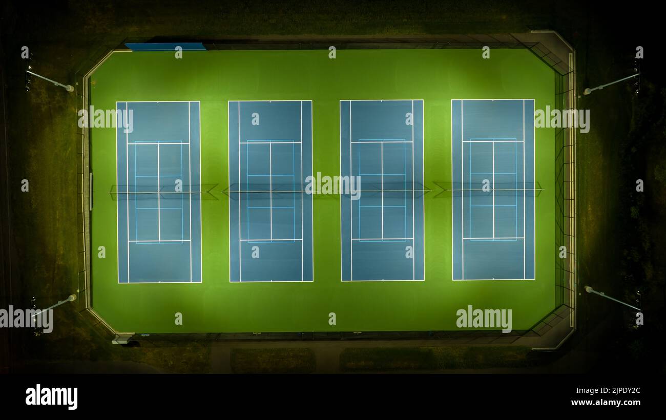 Abendliches Luftvideo von blauen Tennisplätzen im Freien mit Pickleball-Linien und eingeschaltetem Licht. Stockfoto