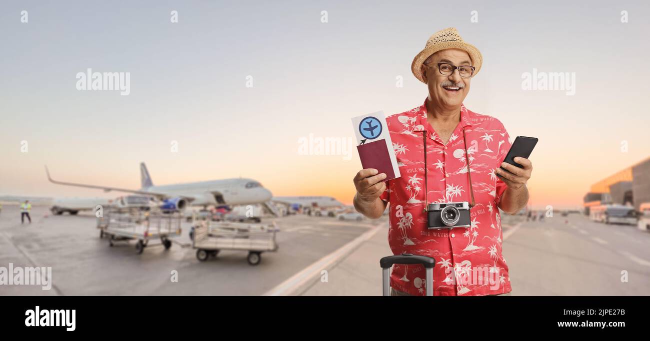 Reifer männlicher Tourist mit einem Reisepass und einem Flugticket an einem Flughafen-Vorfeld Stockfoto