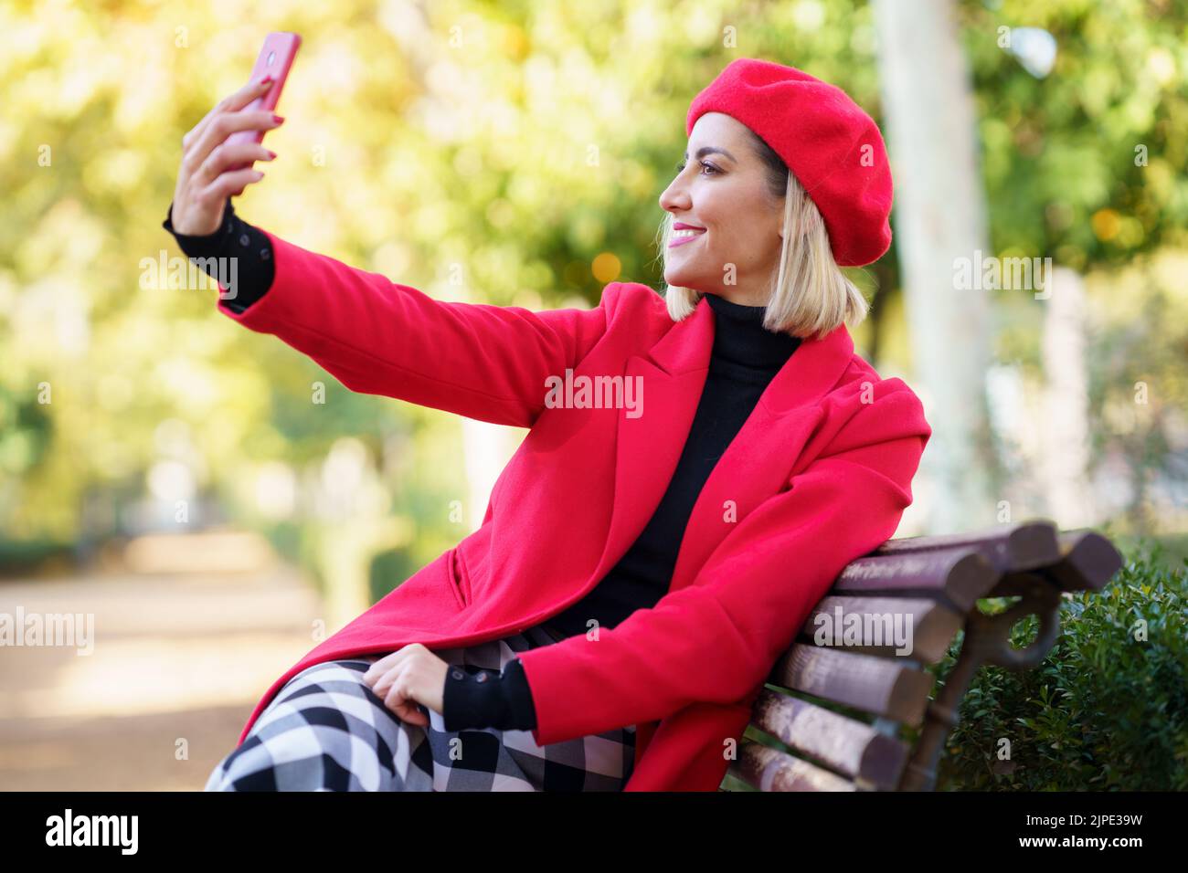 Fröhliche Frau nimmt Selfie im Park mit roten Kleidern. Stockfoto