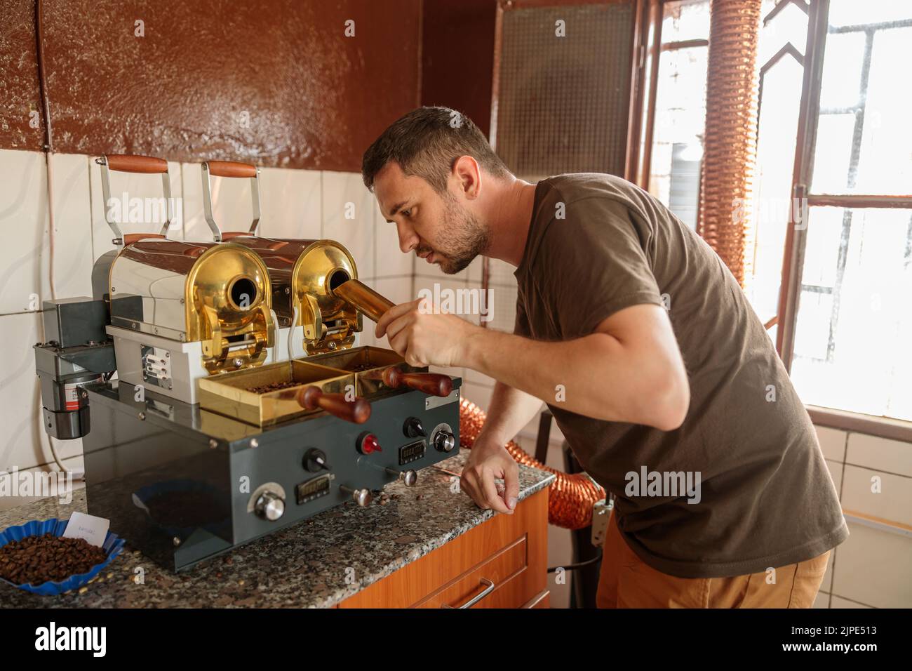 Mann, der Kaffeebohnen in die Kaffeemaschine in der Fabrik gießt Stockfoto