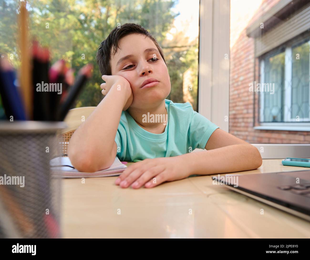Der Schuljunge schaut dejectedly auf den Laptop-Bildschirm und hat Schwierigkeiten, Informationen während des Online-Unterrichts mit dem Lehrer zu erkennen Stockfoto