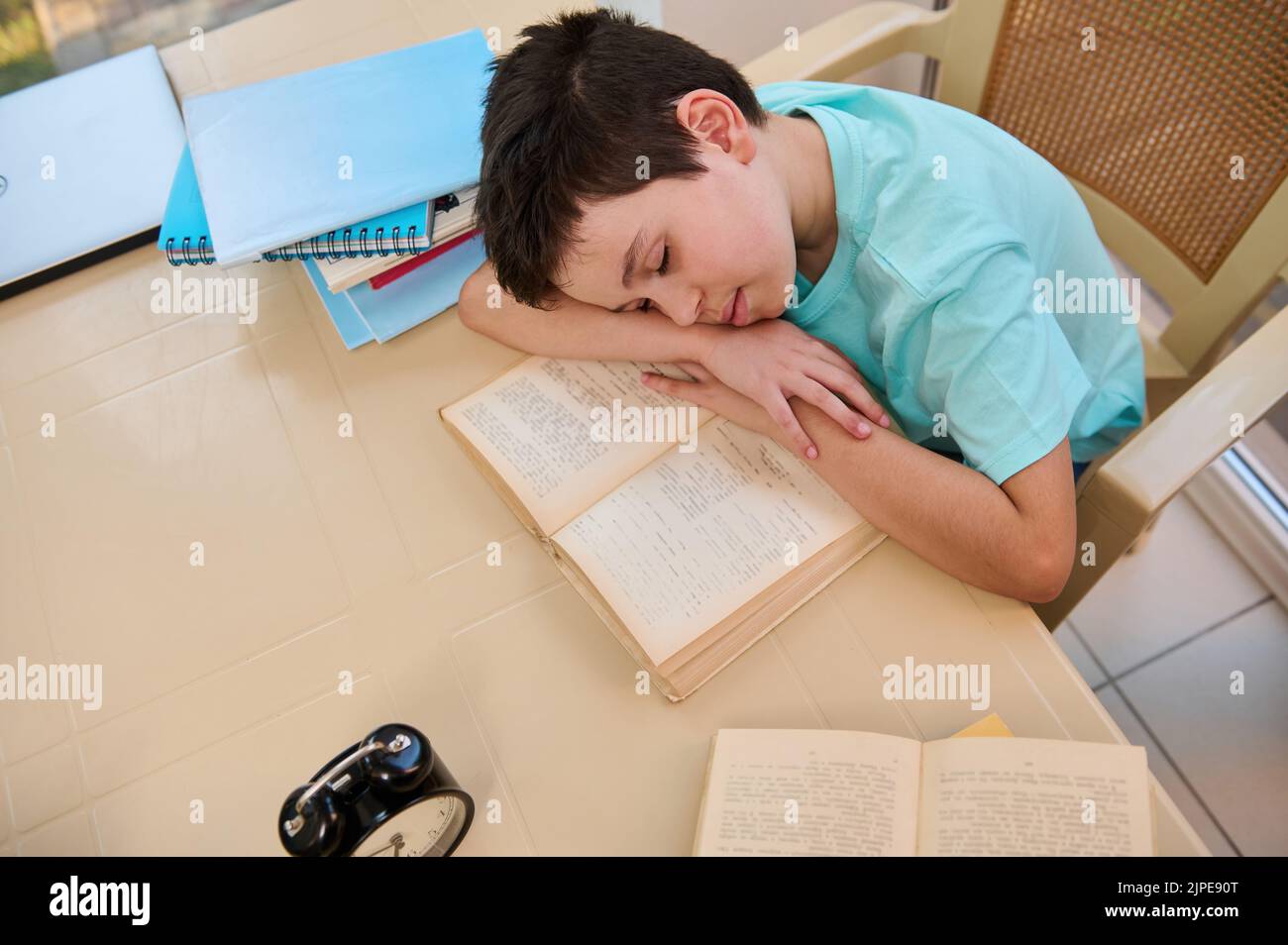 Draufsicht auf einen müden, schläfrigen Schuljungen, der während der Hausaufgaben auf einem Lehrbuch einschläft. Heimschooling. Zurück zur Schule Stockfoto