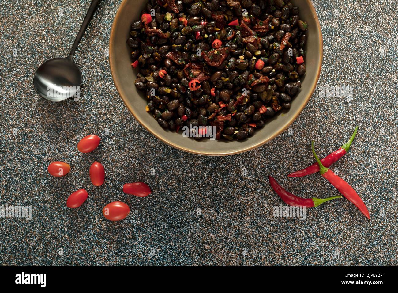 Schwarze Bohnen mit getrockneten Tomaten und roten Cayennepfeffer in einer braunen Schale. Stockfoto