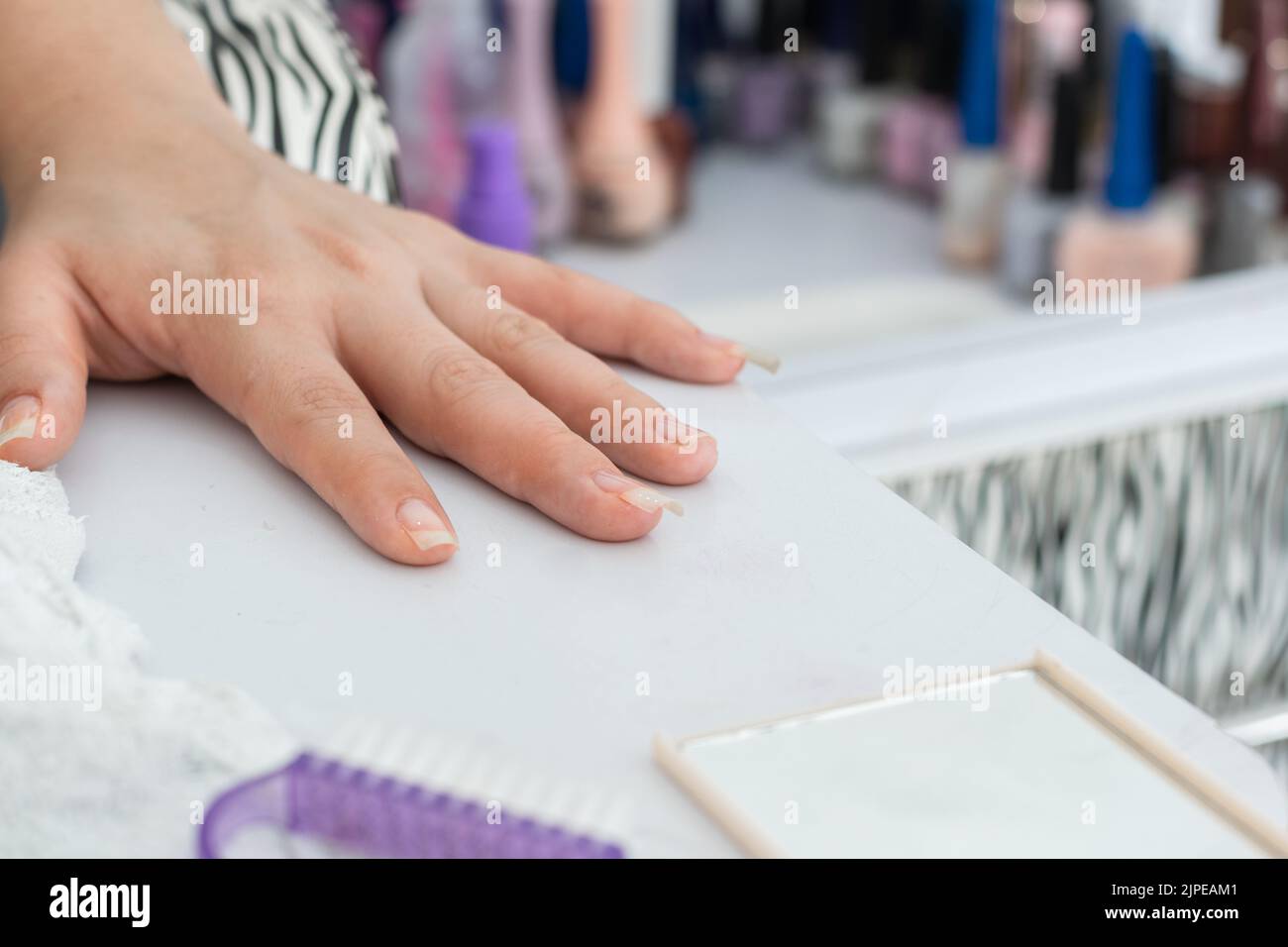 Detail der lateinischen Mädchenhand, auf dem Maniküre-Tisch platziert, bereit zu malen und die Nägel zu schmücken. Im Hintergrund viele farbige Polituren. Stockfoto