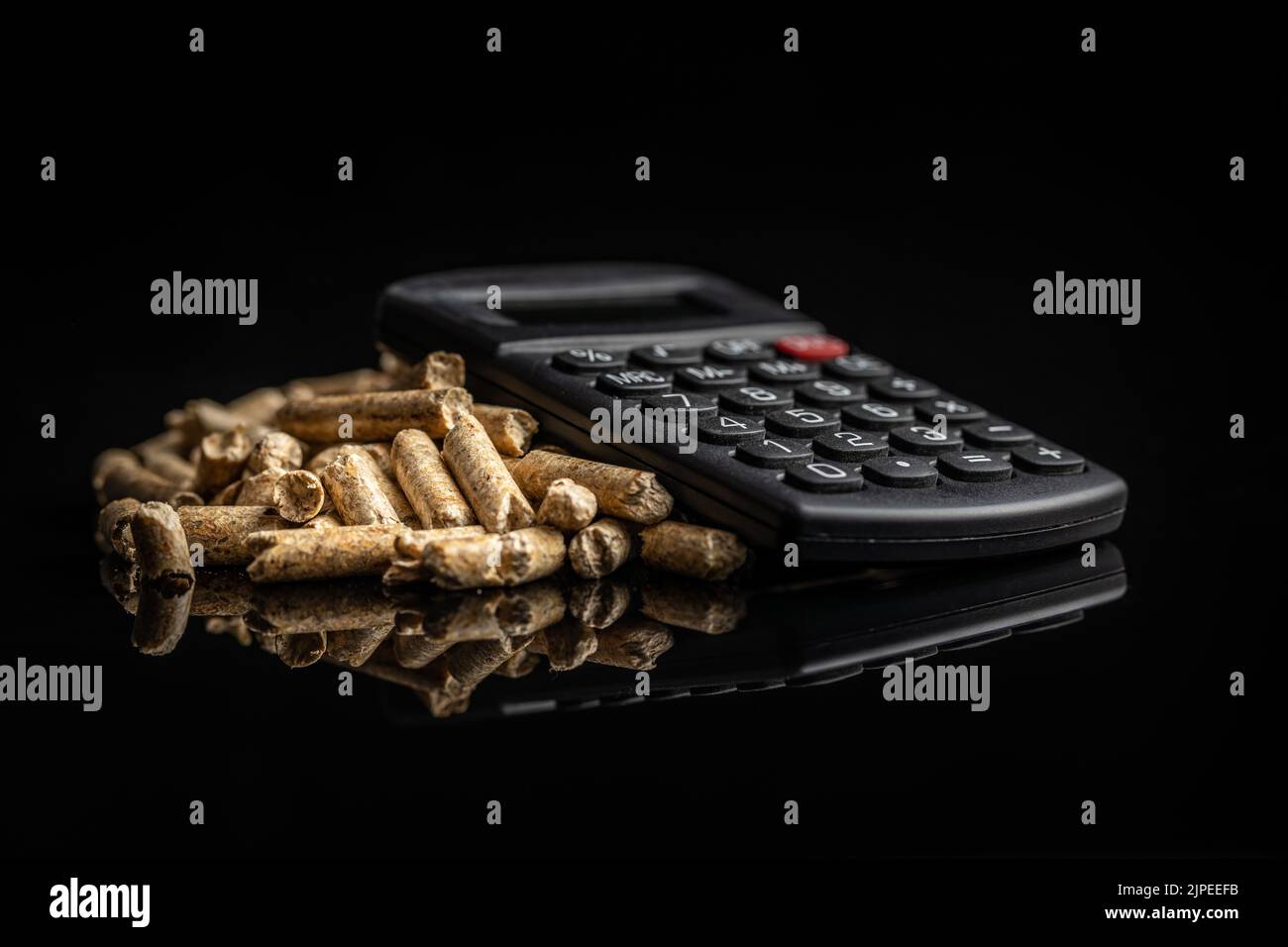 Holzpellets und Taschenrechner auf schwarzem Hintergrund. Das Konzept der Bezahlung für Heizung. Stockfoto