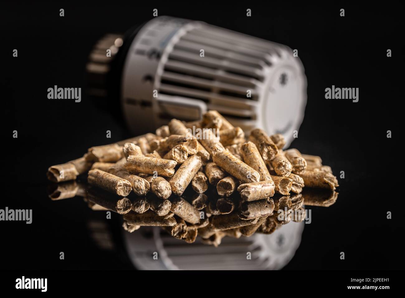 Holzpellets und Thermostat-Ventilkopf auf schwarzem Hintergrund. Biomasse - Erneuerbare Wärmequelle. Stockfoto