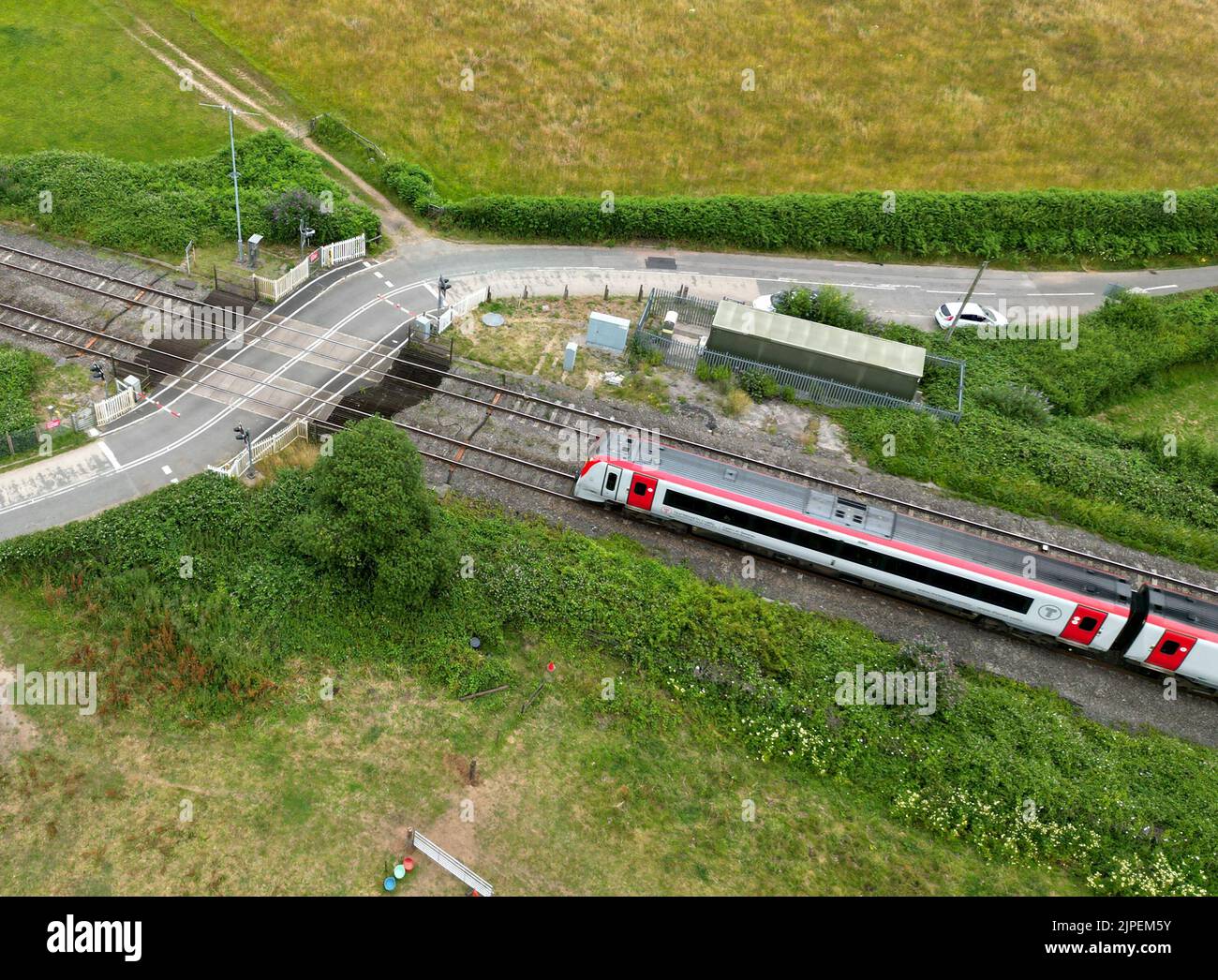 Wale of Glamorgan, Wales - Juli 2022: Luftaufnahme eines Pendlerzuges, der sich einem ländlichen Bahnübergang nähert. Der Zug wird von Transport for Wales betrieben Stockfoto