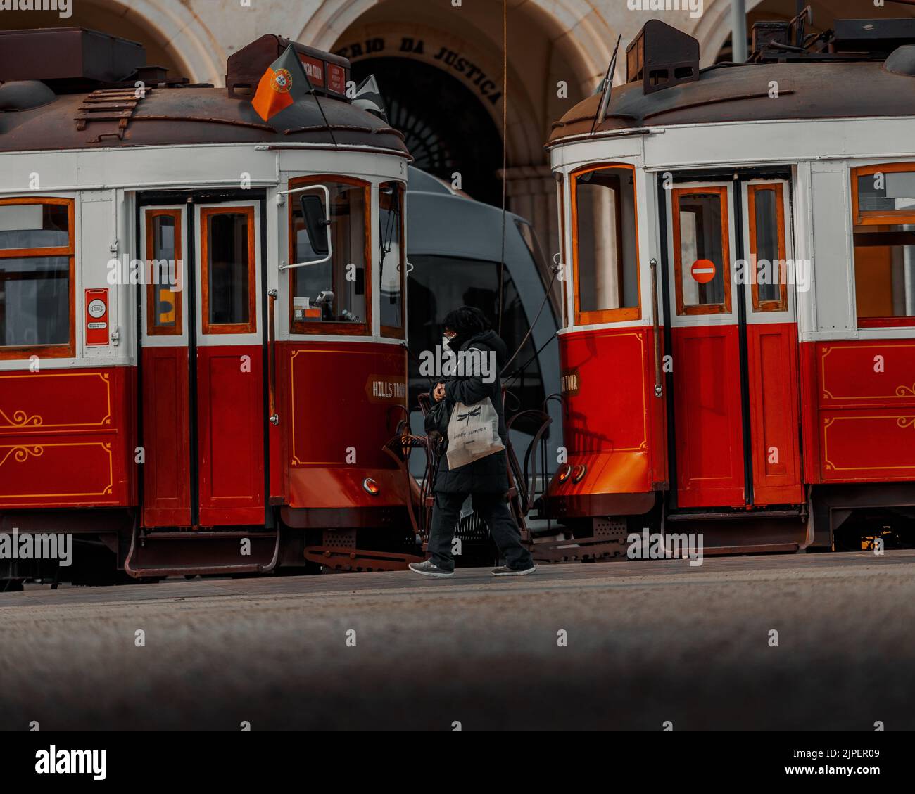 Eine Nahaufnahme von zwei roten Straßenbahnen, die gegeneinander laufen, mit einer Person, die vor Lissabon vorbeiläuft Stockfoto