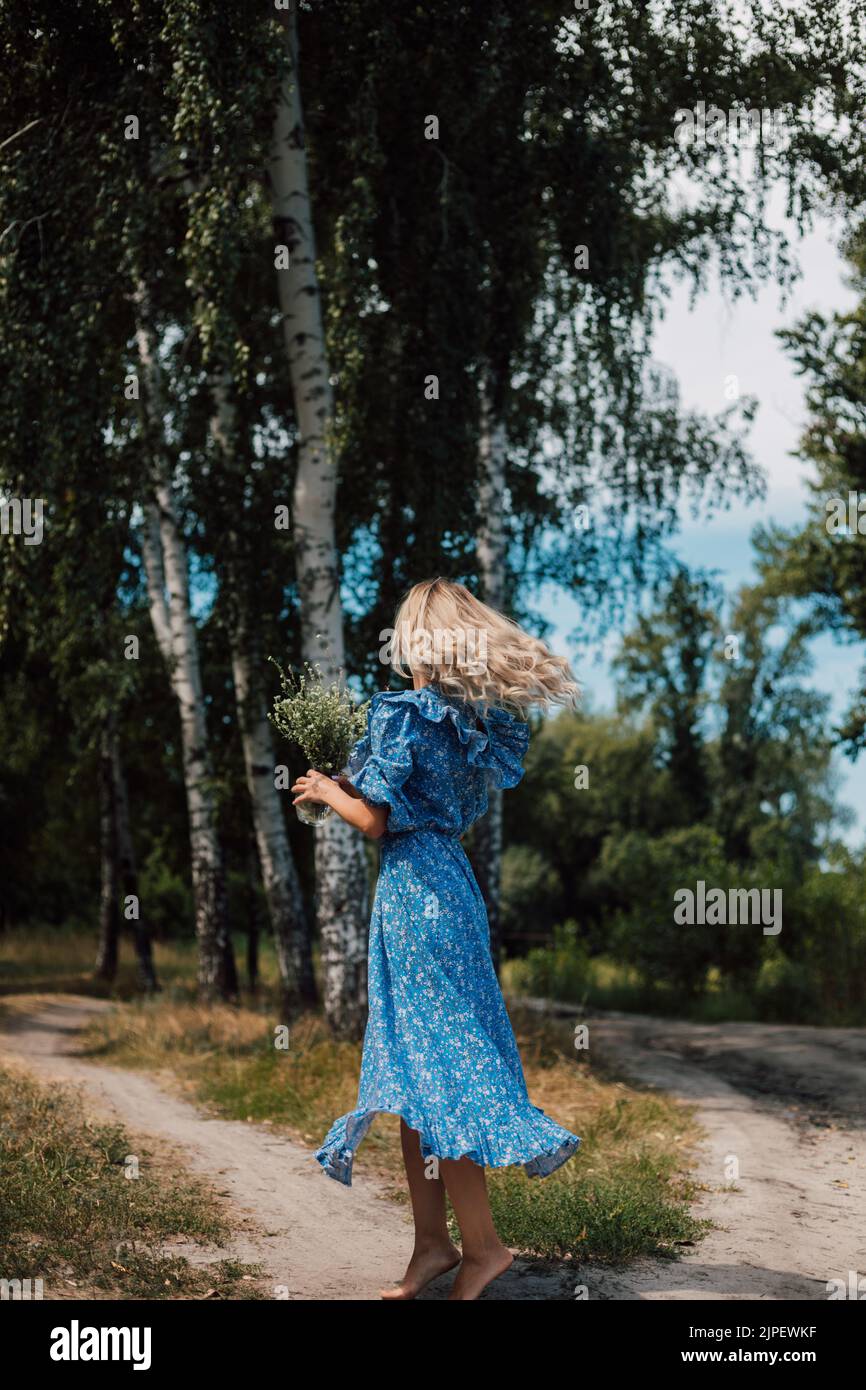 Eine junge schöne Frau steht mit ihrem Rücken im Wald in einem langen blauen Kleid Stockfoto