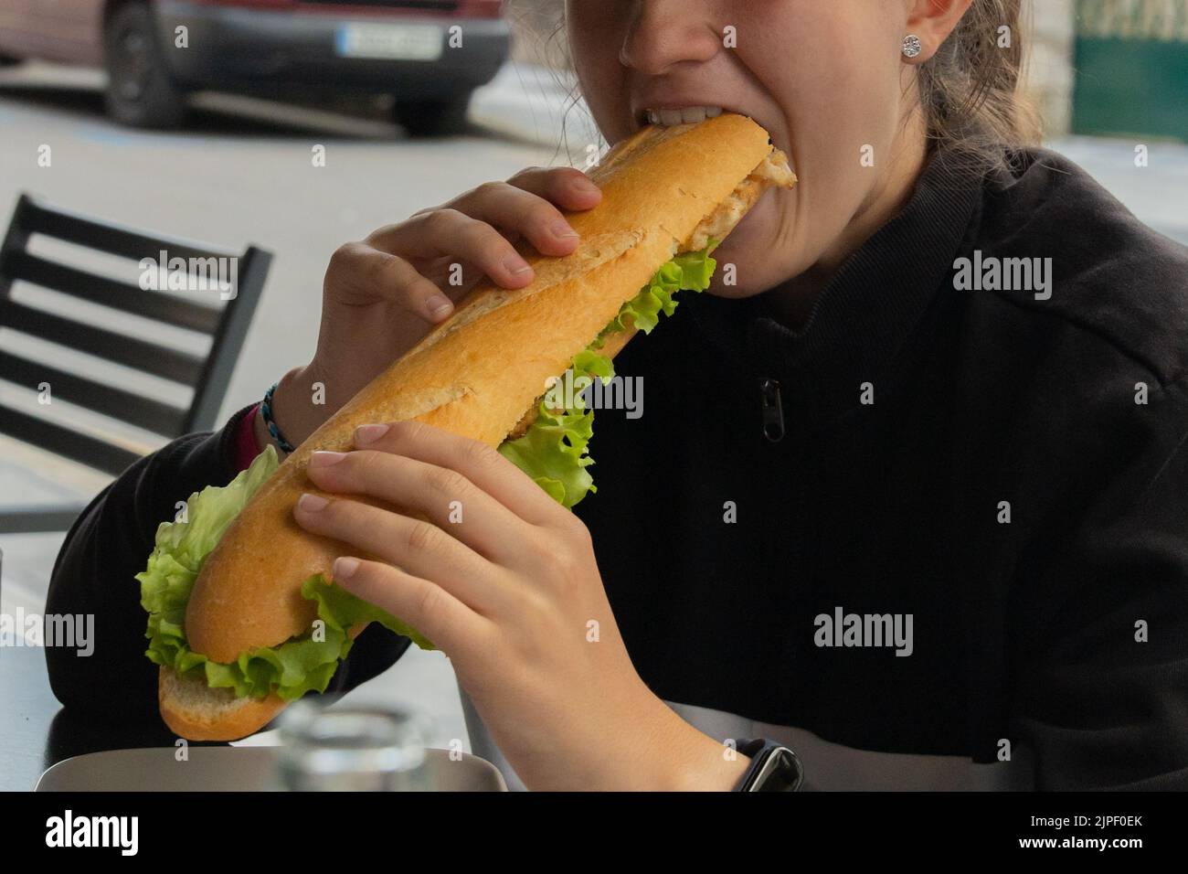 Detail einer jungen Frau, die ein Sandwich mit rustikalem Brot mit paniertem Fleisch und vegetarischem Salat isst Stockfoto