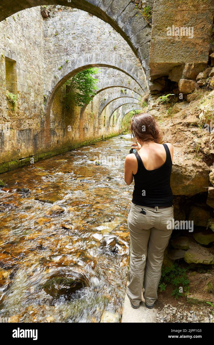 Frau fotografiert die steinernen Torbögen über dem Fluss Legartza an der Real Fábrica de Armas y Municiones de Orbaiceta (Orbaizeta, Aezkoa, Navarra, Spanien) Stockfoto