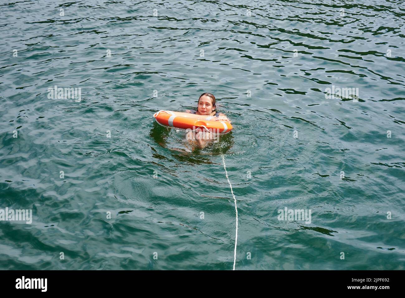 Ein junges Mädchen, das sich in einer Lifebuoy im Meer unter dem Sonnenlicht entspannt Stockfoto