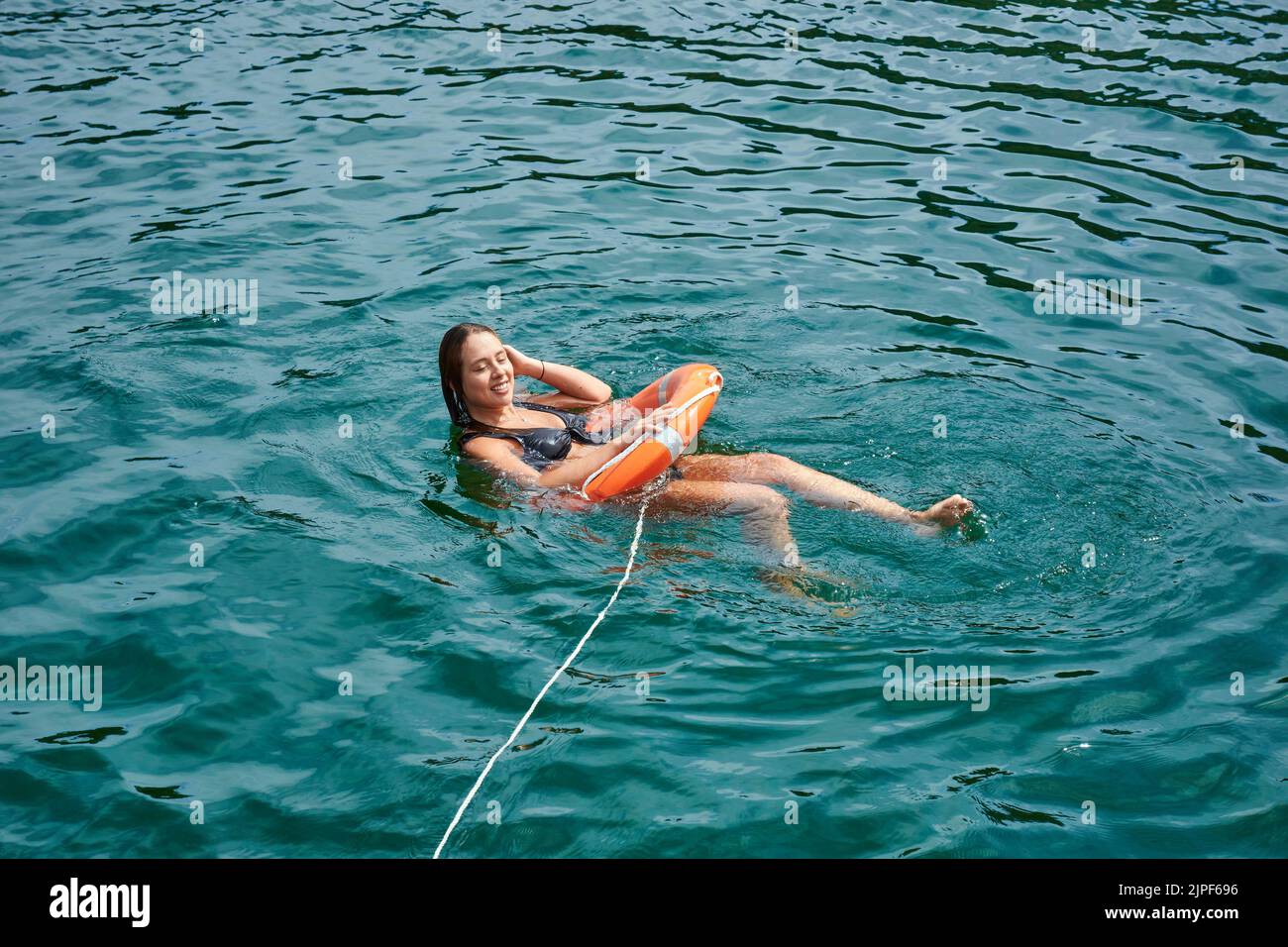 Ein junges Mädchen, das sich in einer Lifebuoy im Meer unter dem Sonnenlicht entspannt Stockfoto