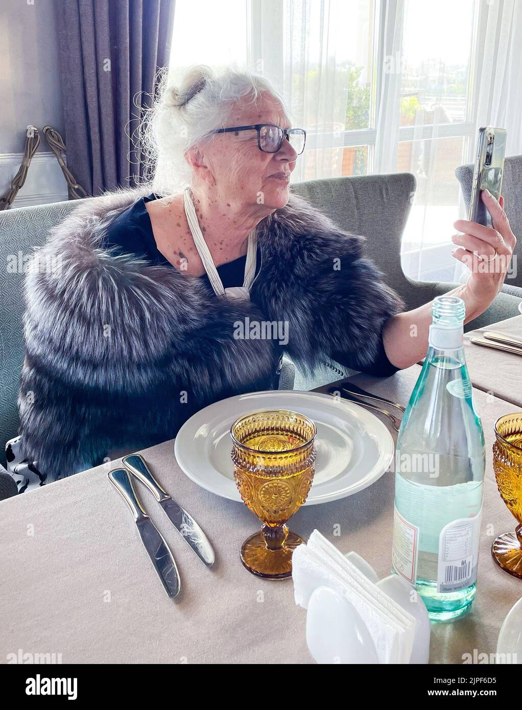 Eine wunderschöne grauhaarige ältere Frau in einem Restaurant nutzt das Smartphone. Online-Jubiläumsgrüße. Stockfoto