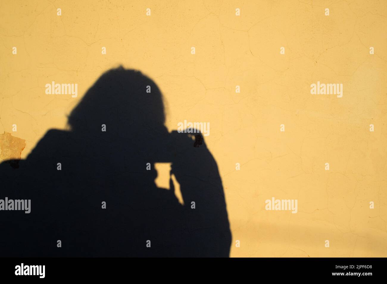 Selfie einer Fotografin in Form eines menschlichen Schattens mit einer Kamera auf einem gelben alten schäbigen Wandhintergrund. Speicherplatz kopieren. Stockfoto