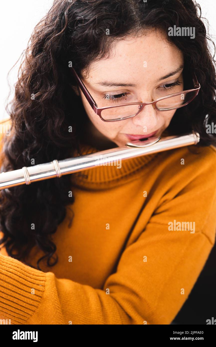 Nahaufnahme einer Brünette, die einen gelben Pullover trägt und eine Querflöte spielt. Vertikal Stockfoto
