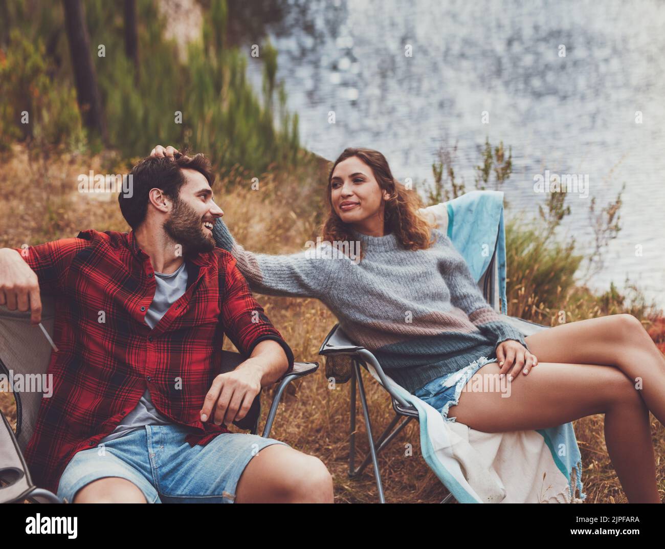 Anhängliches junges Paar, das auf ihrem Campingplatz sitzt. Romantisches junges Paar, das eine gute Zeit auf einem Campingurlaub hat. Stockfoto