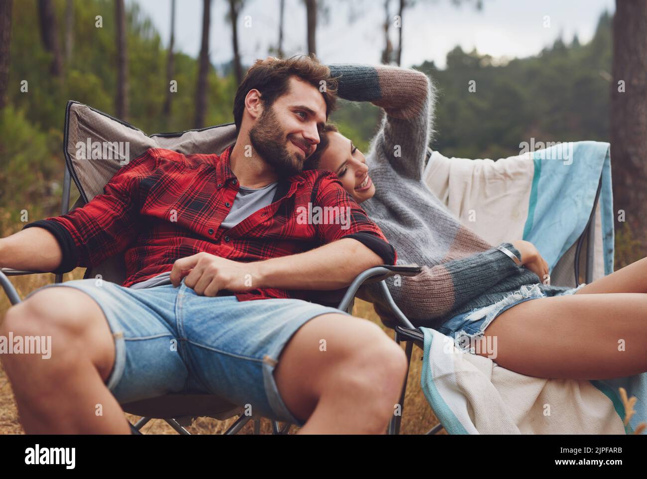 Liebevolles junges Paar, das auf einem Stuhl auf ihrem Campingplatz sitzt. Glücklicher junger Mann und Frau, die in der Natur campen. Stockfoto
