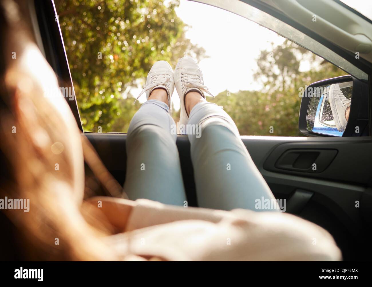 Entspannt, zufrieden und glücklich Frau entspannen, während Sie den sonnigen Morgen im Auto genießen. Rückansicht einer Frau mit den Füßen aus ihrem Fenster, die eine Pause einnahm Stockfoto