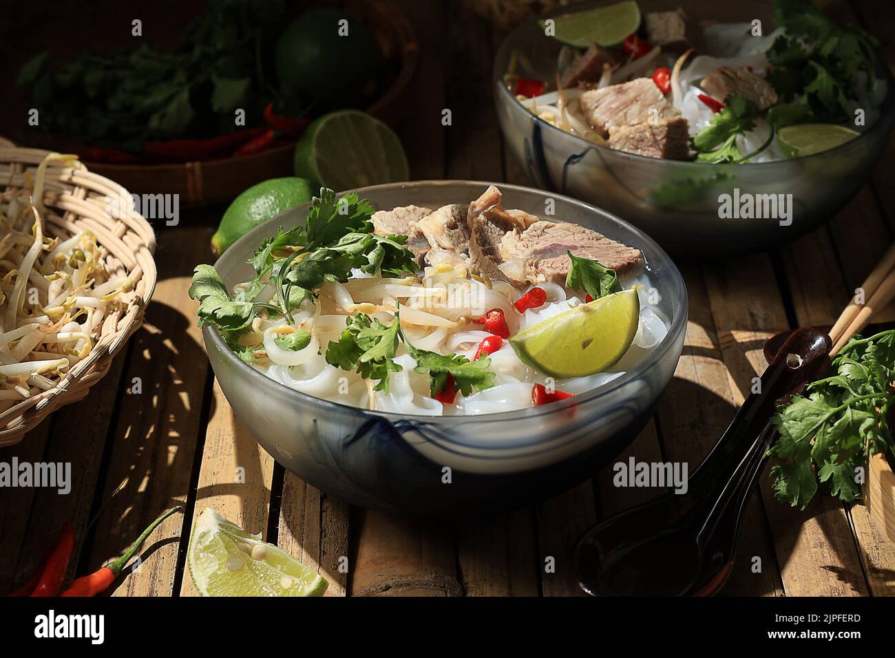 Vietnamesische Reisnudelsuppe Pho Bo mit Rindfleisch auf einem Bambustisch. Belag mit gehacktem Chili, Limette, Korianderblatt und Sprout Stockfoto