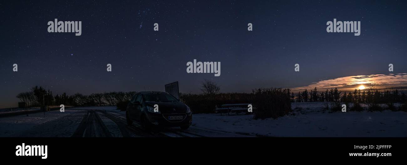 Eine späte Nacht auf einem verschneiten Feld mit Sternen und dem Mond im Hintergrund Stockfoto