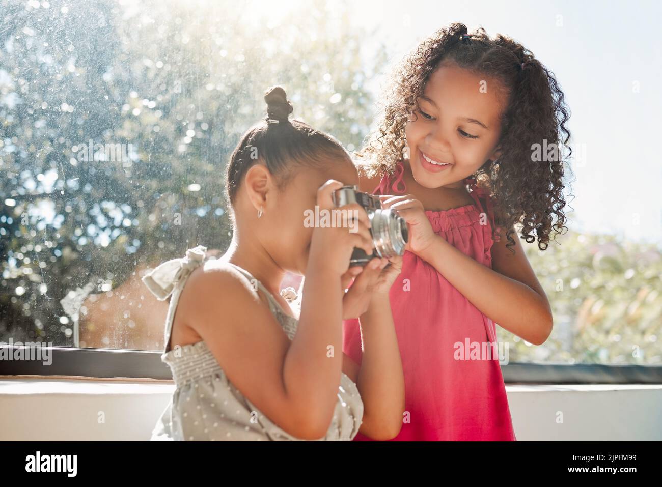 Niedliche Schwestern verbinden sich, machen Fotos mit der Kamera zu Hause, lächeln, während sie verspielt und neugierig sind. Kleine Mädchen spielen, Spaß haben zusammen, genießen Stockfoto