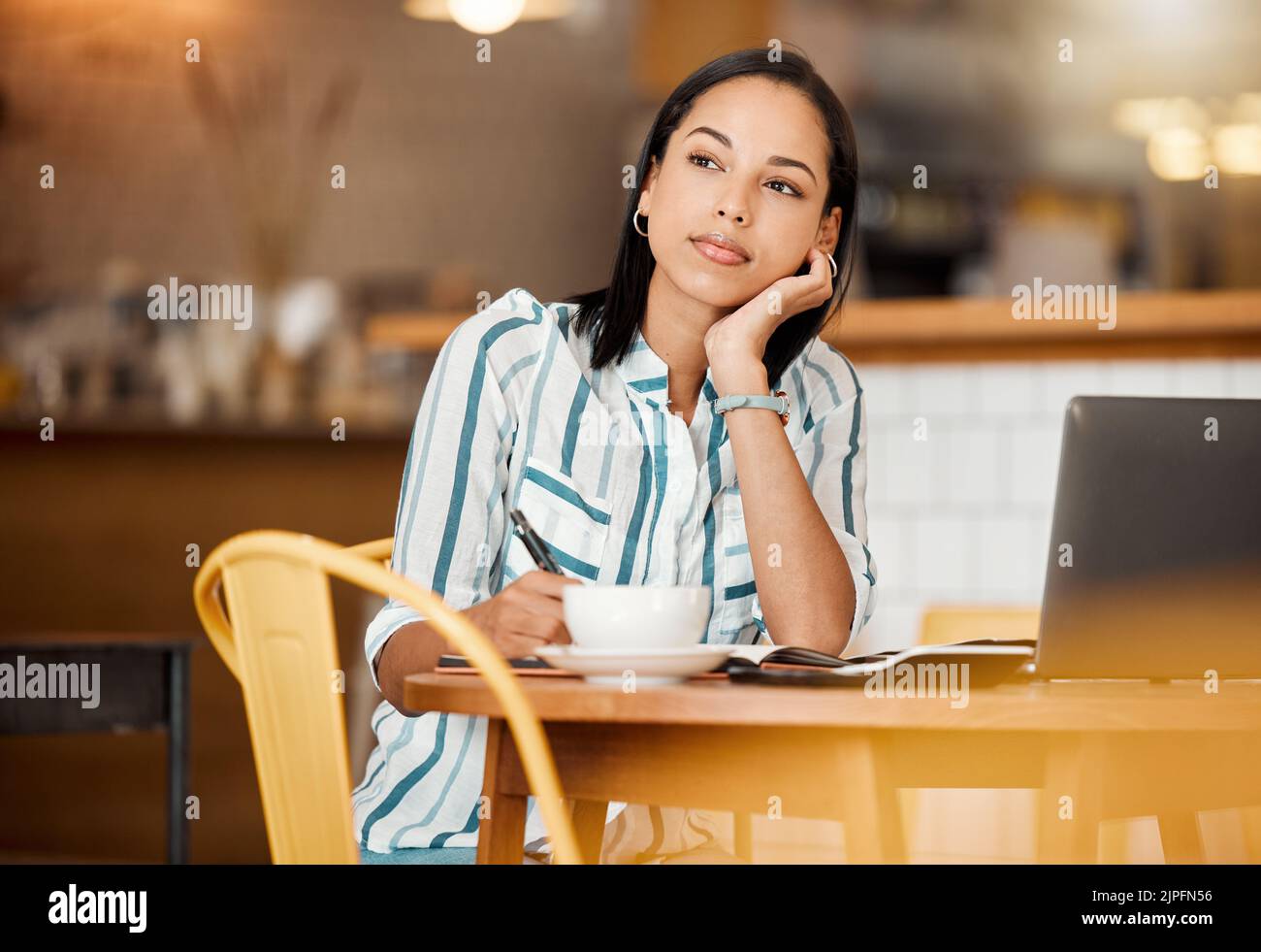 Denkende, wundernde und planende Frau, die einen Kaffee trinken möchte, während sie im Café aus der Ferne am Laptop arbeitet. Freiberufliche Schriftstellerin Tagträumen, denken über ein Stockfoto