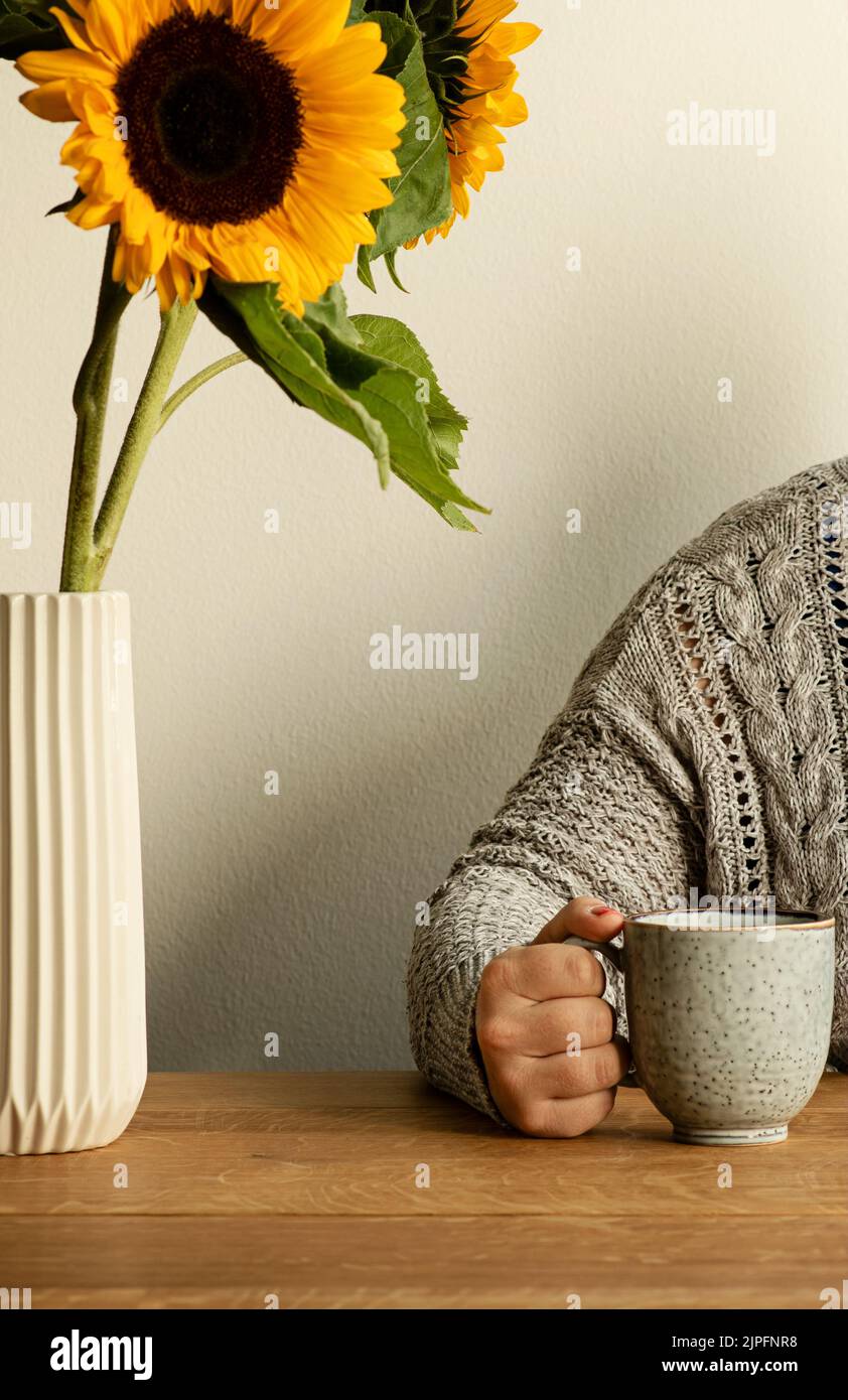 Stillleben mit schönen Sonnenblumen in einer Vase und unkenntlich Frau in einem gemütlichen Strickpullover Kaffee trinken an Holztisch. Stockfoto