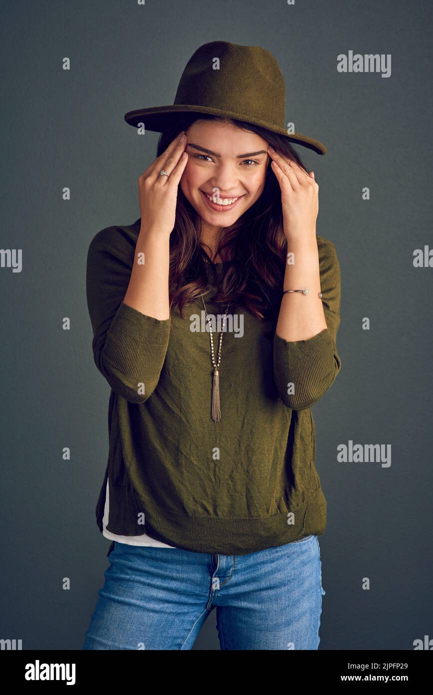 Sogar Hüte sehen gut aus. Studioaufnahme einer fröhlichen jungen Frau, die mit einem Hut posiert, während sie vor einem dunklen Hintergrund steht. Stockfoto
