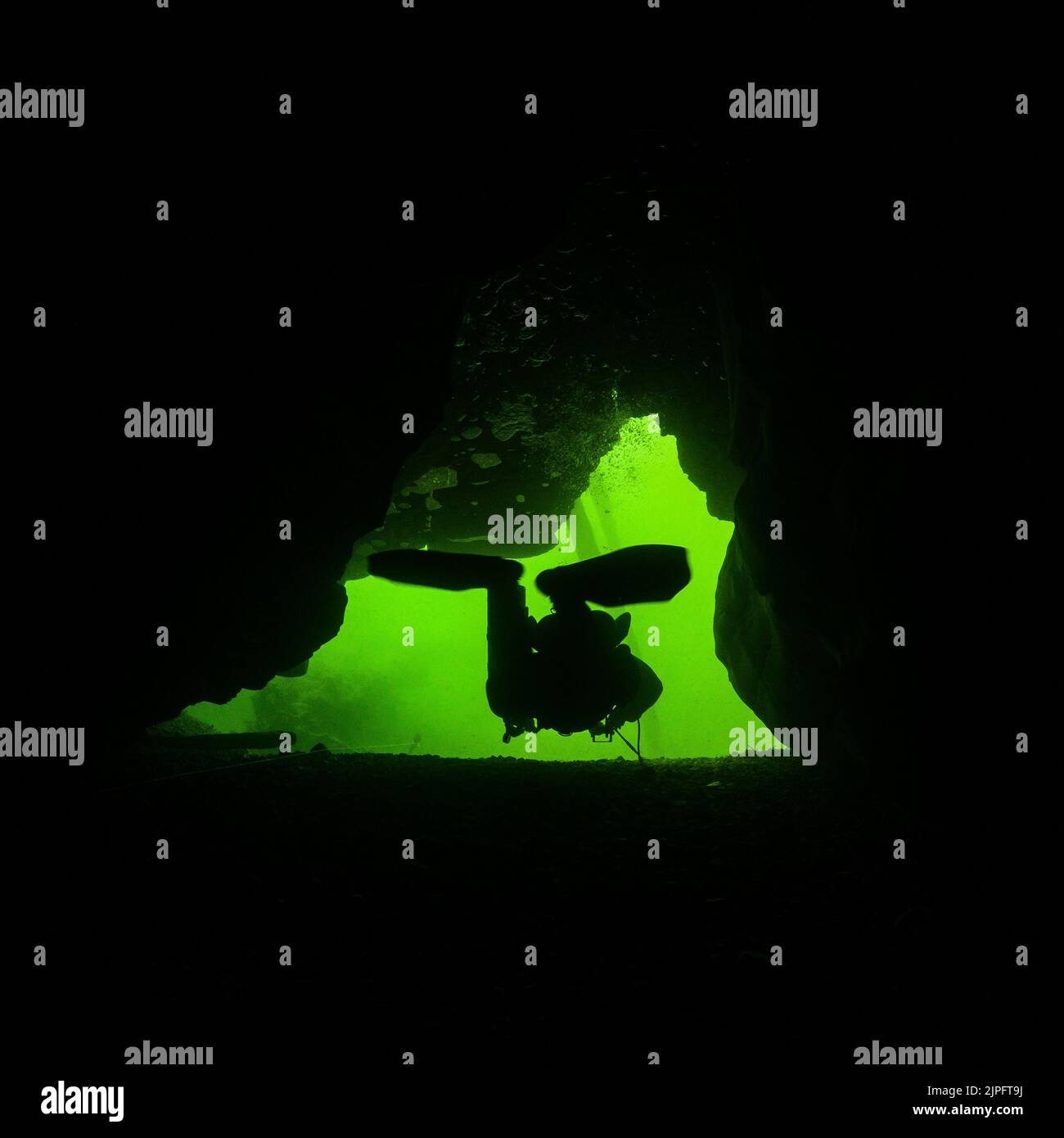 Eine Silhouette eines Tauchers in einer Meereshöhle mit grünem Hintergrund Stockfoto