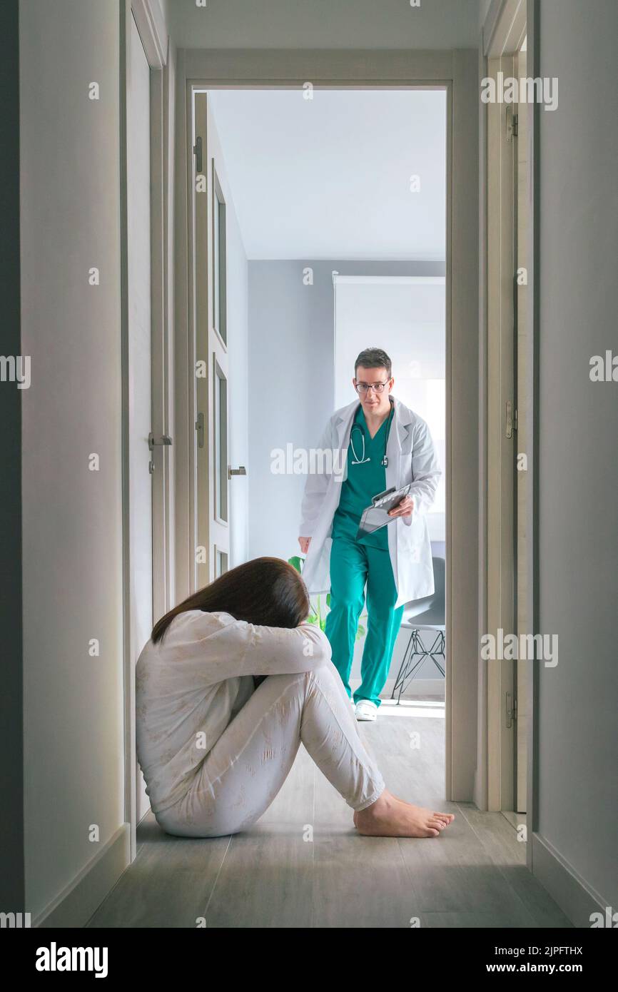Besorgter Arzt läuft, um Patienten mit psychischen Störungen auf dem Boden im Zentrum für psychische Gesundheit zu helfen Stockfoto