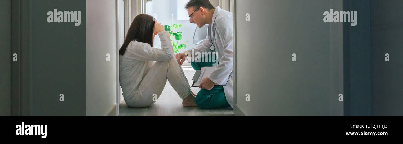 Arzt beruhigt mit Empathie einen Patienten, der auf dem Boden eines Zentrums für psychische Gesundheit sitzt Stockfoto