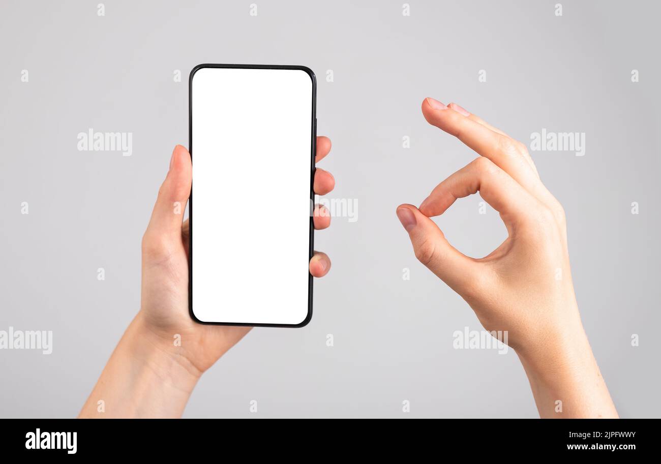 Frau hält Handy-Mockup und zeigt ok Geste. Anwendung, Website-Empfehlung, Genehmigung. Android-Vorlage mit leerer Anzeige. Hoher pH-Wert Stockfoto