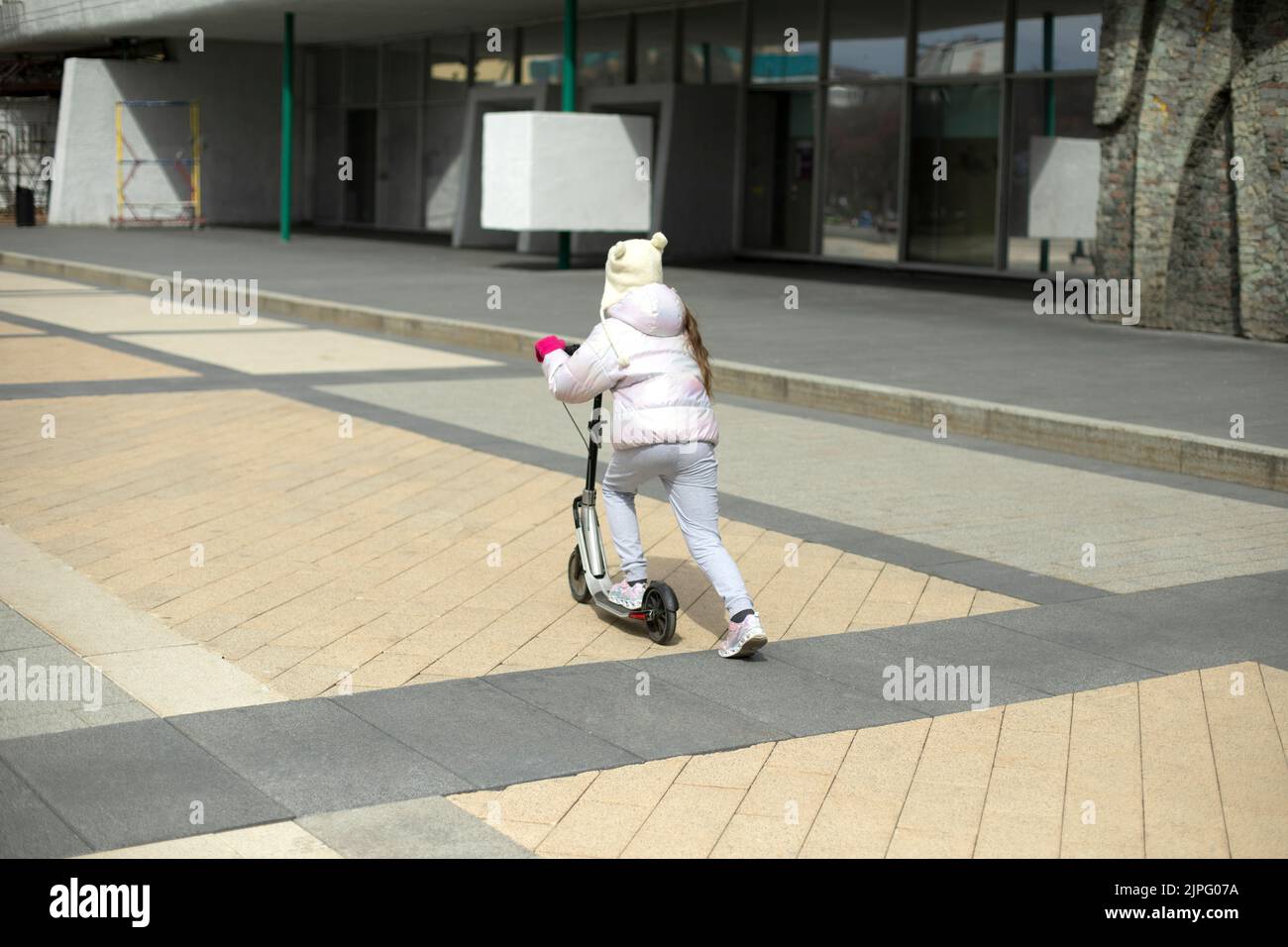 Kind auf dem Roller. Mädchen reitet um den Platz herum. Das Kind reist mit einem mechanischen Transport. Kinder in der Stadt. Stockfoto