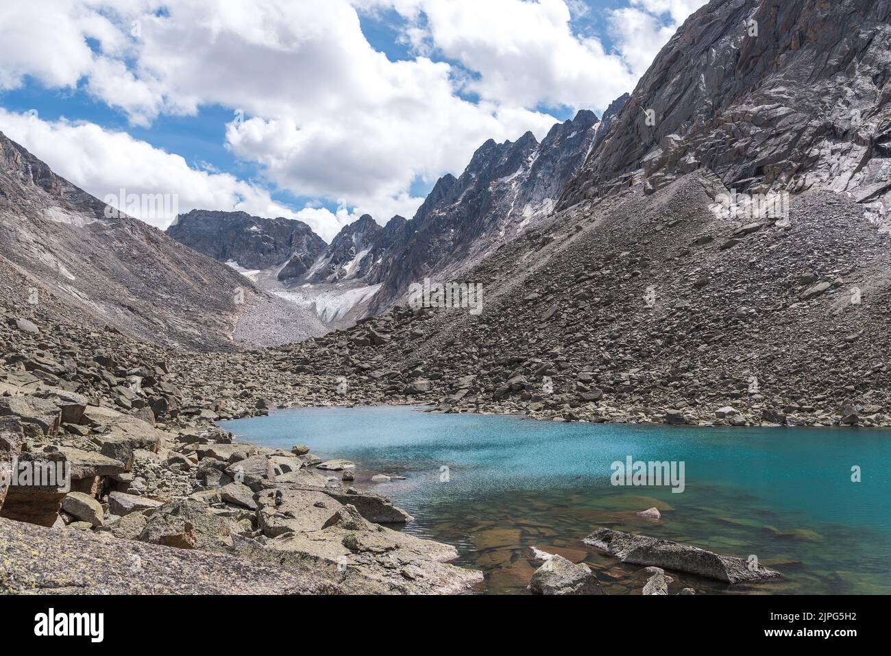 Atemberaubende Sommer-alpine Landschaft mit einem Gletscher, scharfen Felsen, Steinen und einem See mit türkisfarbenem Wasser gegen einen blauen Himmel und Wolken. Altai, Russland Stockfoto