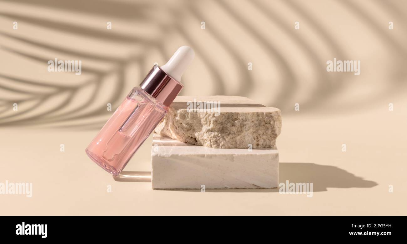 Tropfflasche auf Travertin-Stein in der Nähe von weißen Orchideenblüten und Palmenblatt-Schatten auf hellgelb, Nahaufnahme, Mockup. Hautpflege Beauty-Produkt, essentia Stockfoto