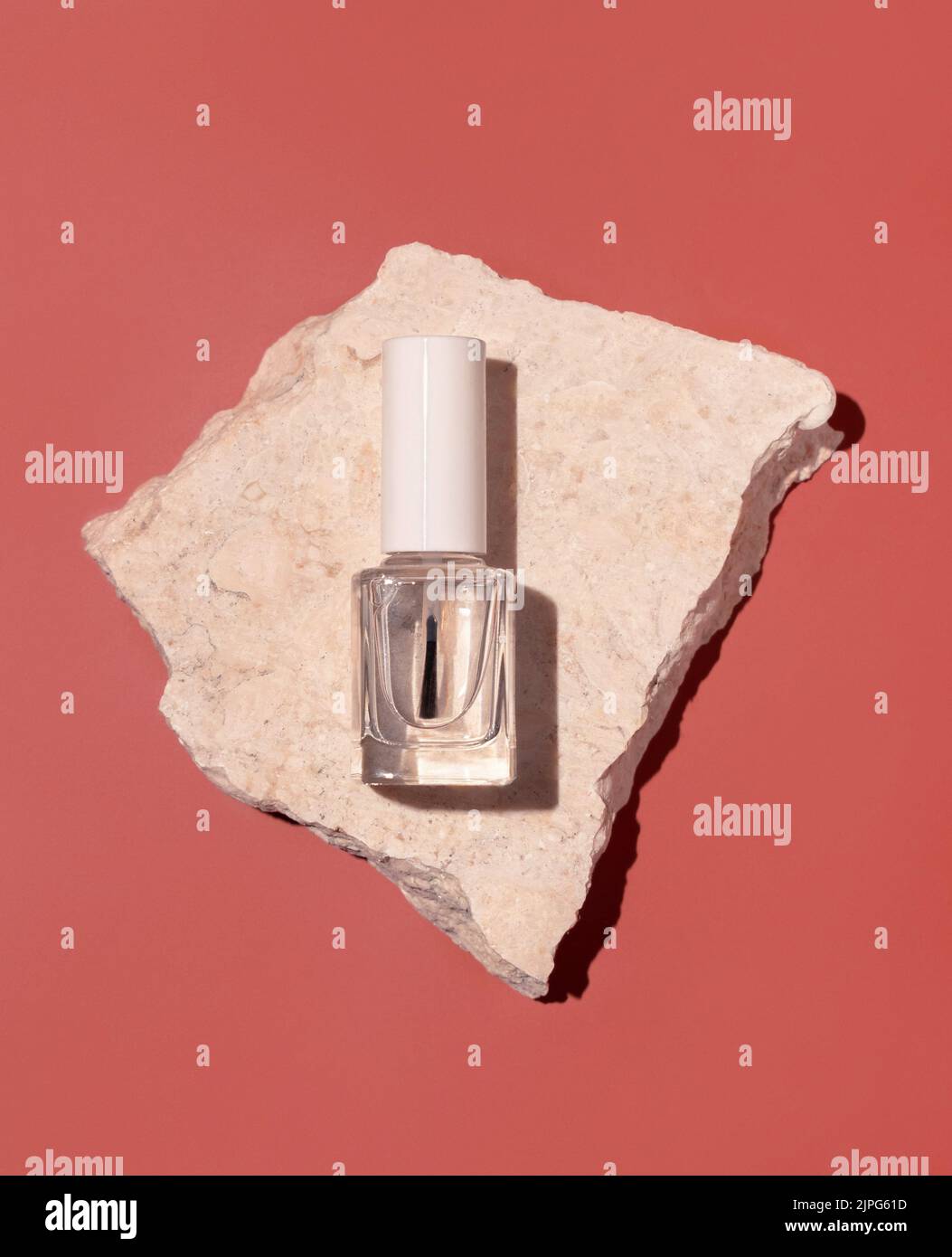 Wiederfüllbare Flasche aus klarem Glas mit Bürstendeckel in der Nähe beigefarbener Travertin-Steine auf rosa, Draufsicht, Mockup. Harter Schatten. Hautpflege Nagel Produkt. Natürliches cosme Stockfoto