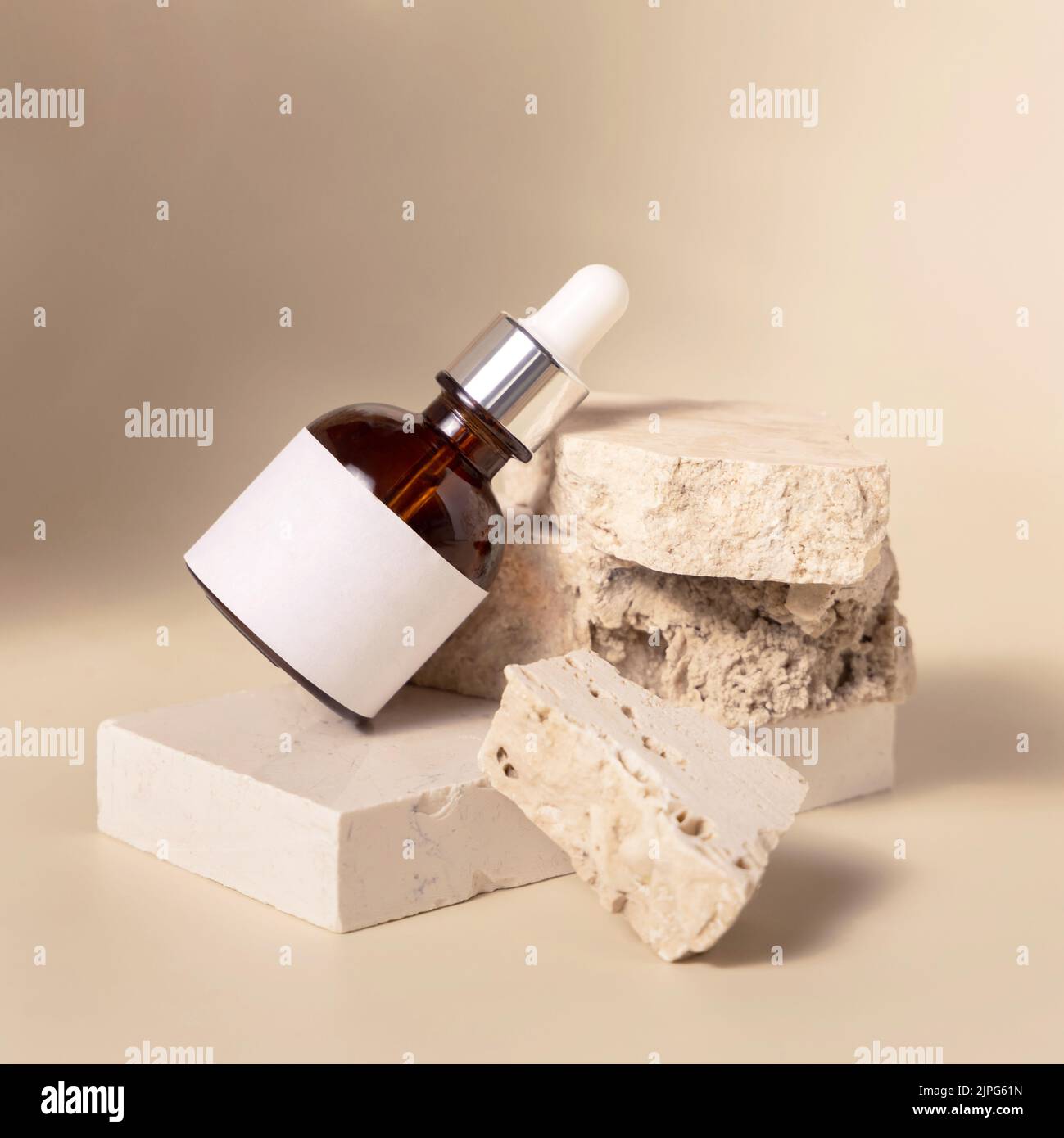 Braune kosmetische Tropfflasche mit unbeschrifteter Aufschrift auf beigen Travertin-Steinen auf hellgelb, Nahaufnahme, Hautpflegeprodukt Mockup. Natürliche Öko-Frien Stockfoto