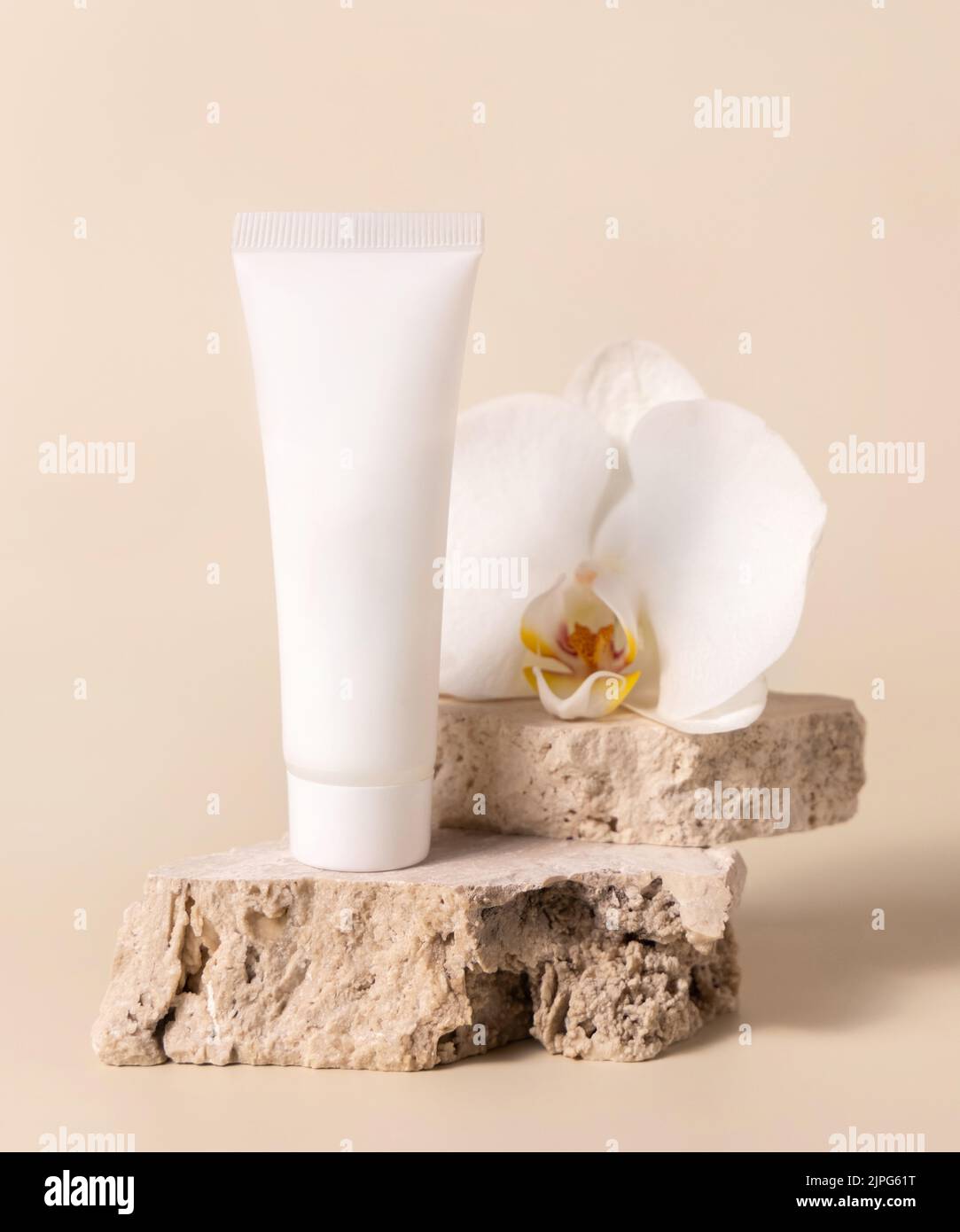 Weiße cremefarbene Röhre auf Travertin-Stein in der Nähe der weißen Orchideenblume auf hellgelb, Nahaufnahme, Mockup. Hautpflege handgemachtes Beauty-Produkt, Creme oder Lotion. Z. B. Stockfoto