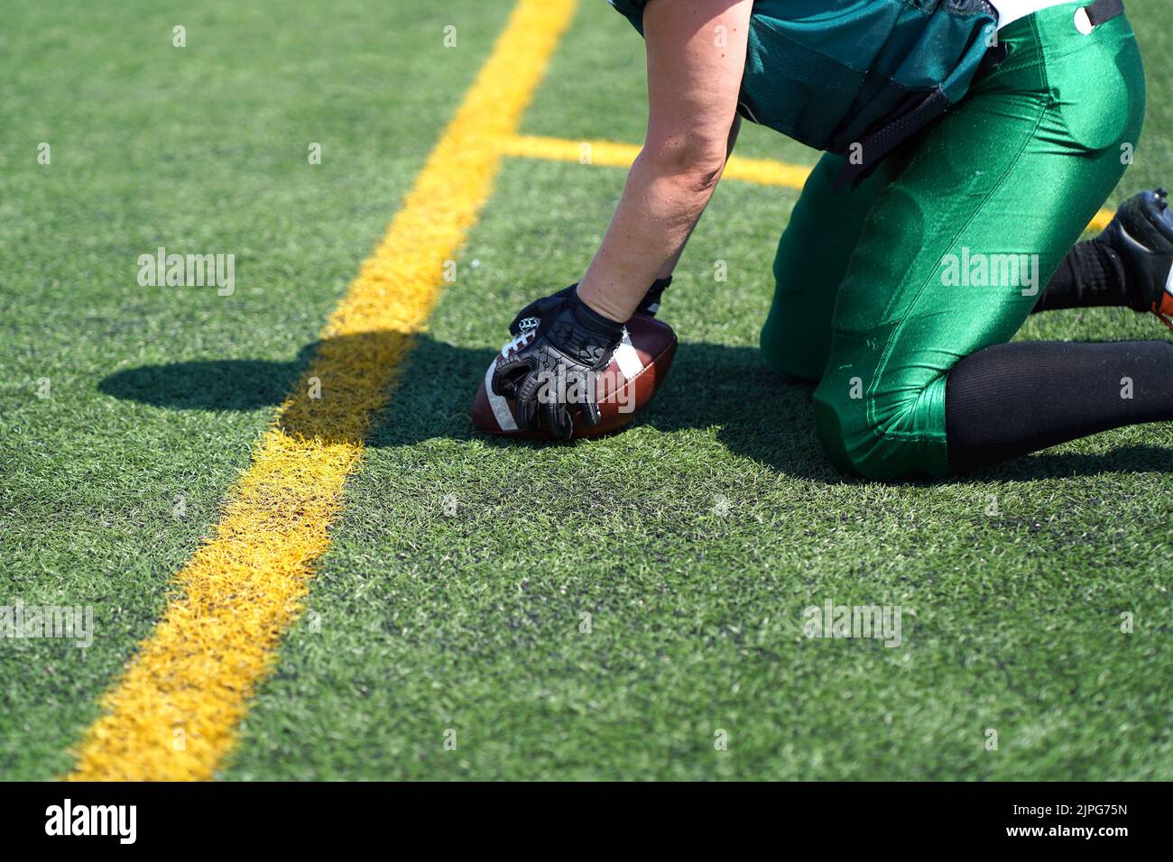 Weiße, mit Handschuhen beulte Hände greifen nach einem Wilson American Football, der auf einem künstlichen Grasfeld rollt Stockfoto