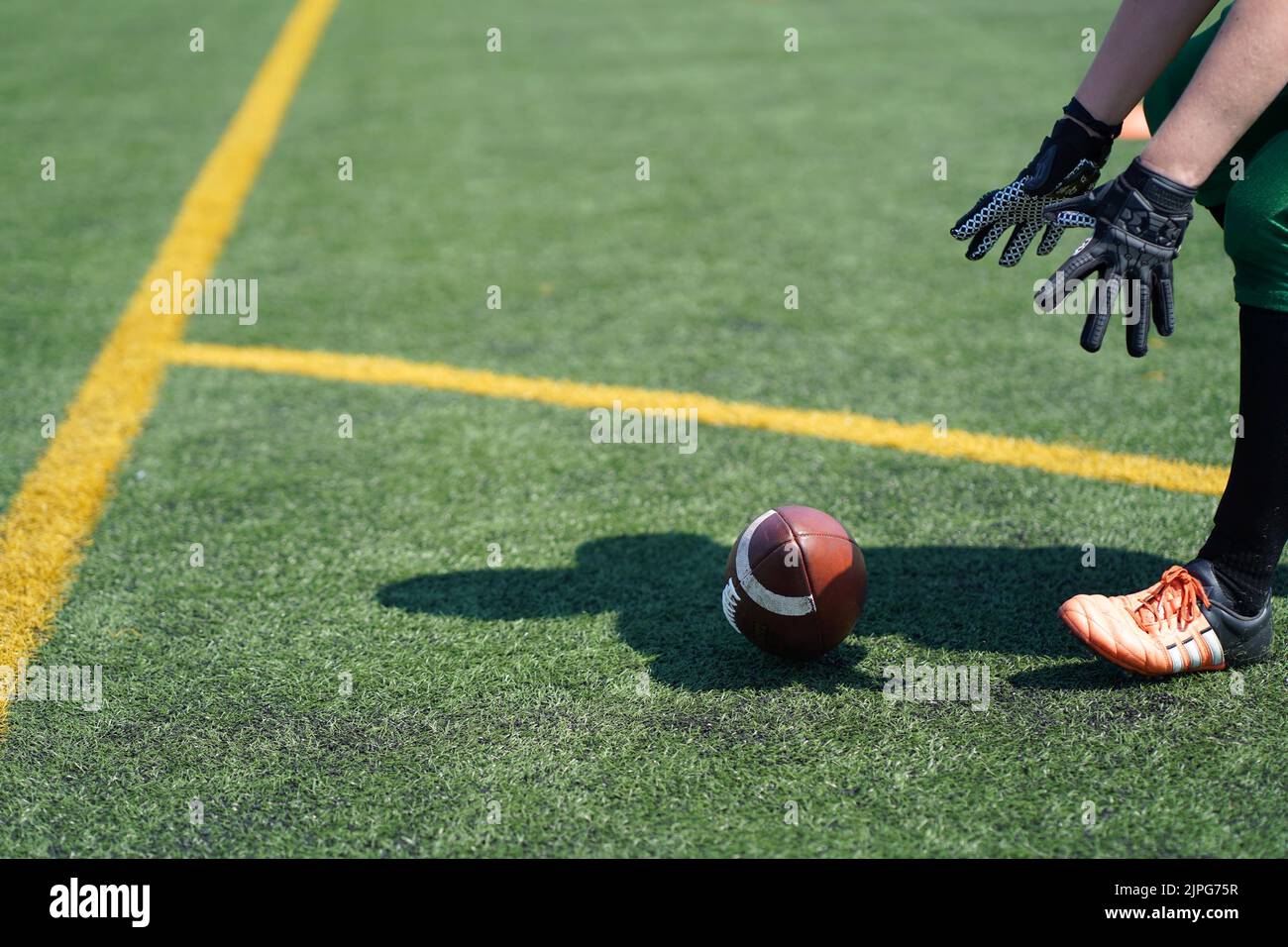 Weiße, mit Handschuhen beulte Hände greifen nach einem Wilson American Football, der auf einem künstlichen Grasfeld rollt Stockfoto