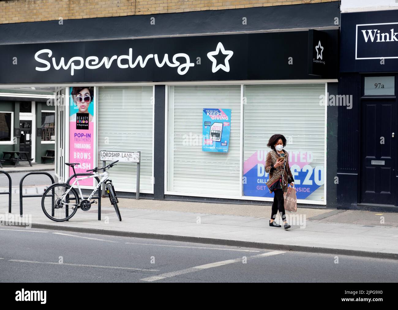 Während der Coronavirus-Sperre (Covid-19) geht eine Frau in einer Gesichtsmaske an Superdrug in Lordship Lane, East Dulwich, South London vorbei. Stockfoto